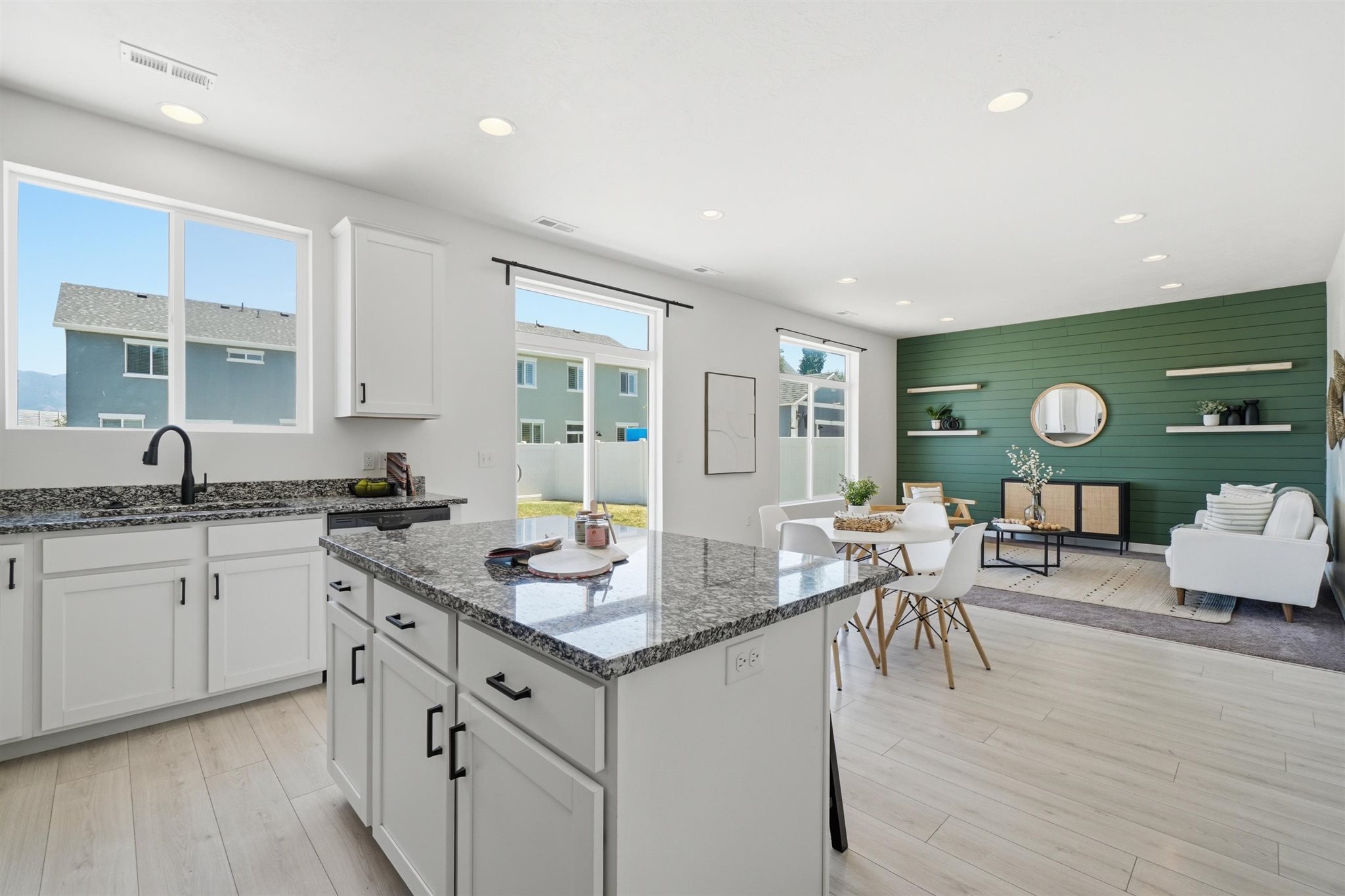 Open-concept living space featuring a kitchen island with stone-finish countertop, white cabinetry with matte black hardware, wood-finish flooring, recessed lighting, and a feature wall with shiplap detailing