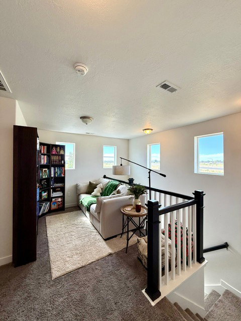 Carpeted loft area featuring a white and black staircase railing, multiple windows, and recessed lighting