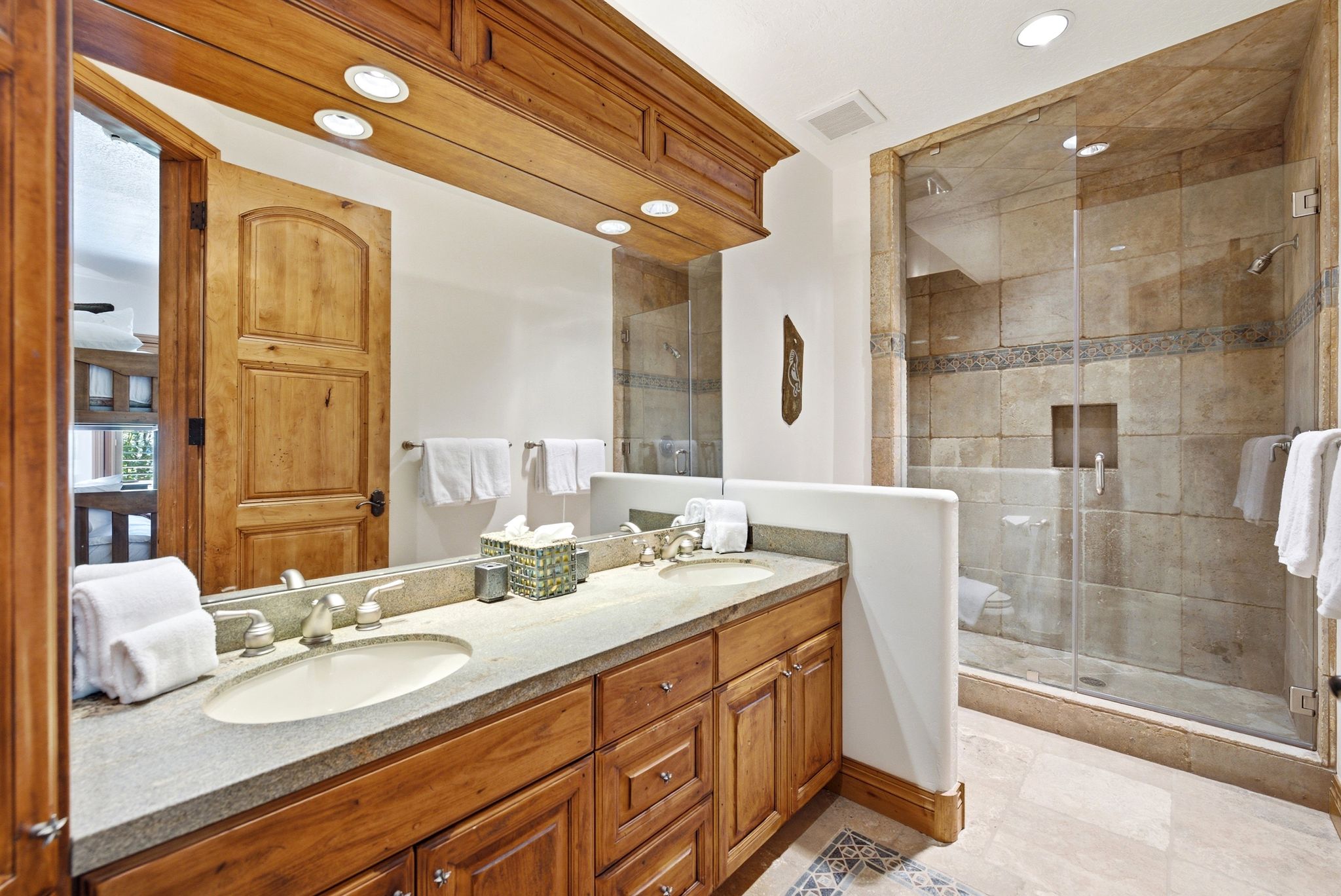 Double vanity with undermount sinks, stone countertop, wood cabinetry, and a glass-enclosed shower with stone tile