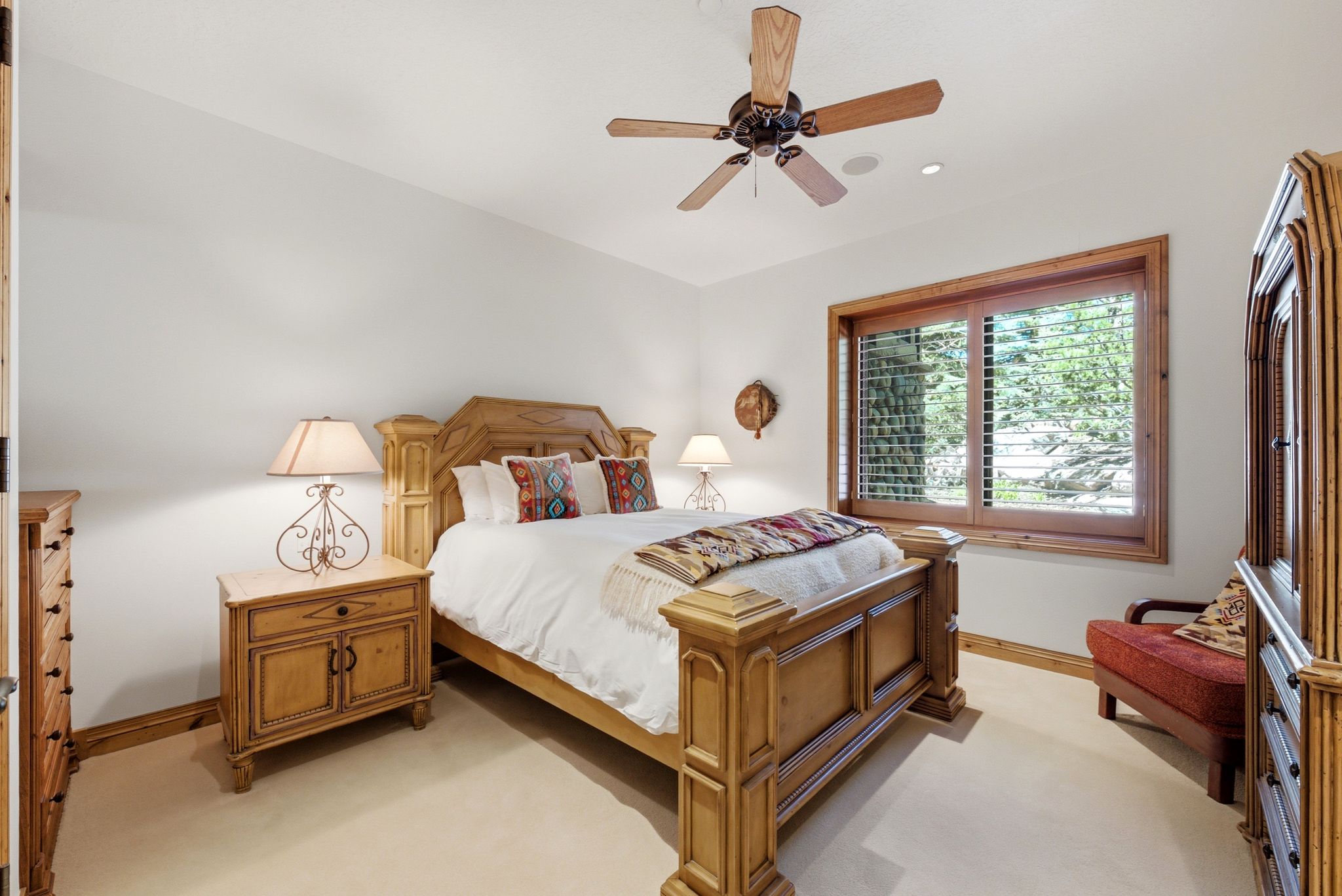 Bedroom featuring a wood-frame window with plantation shutters, wood-finish flooring, and a ceiling fan with integrated lighting