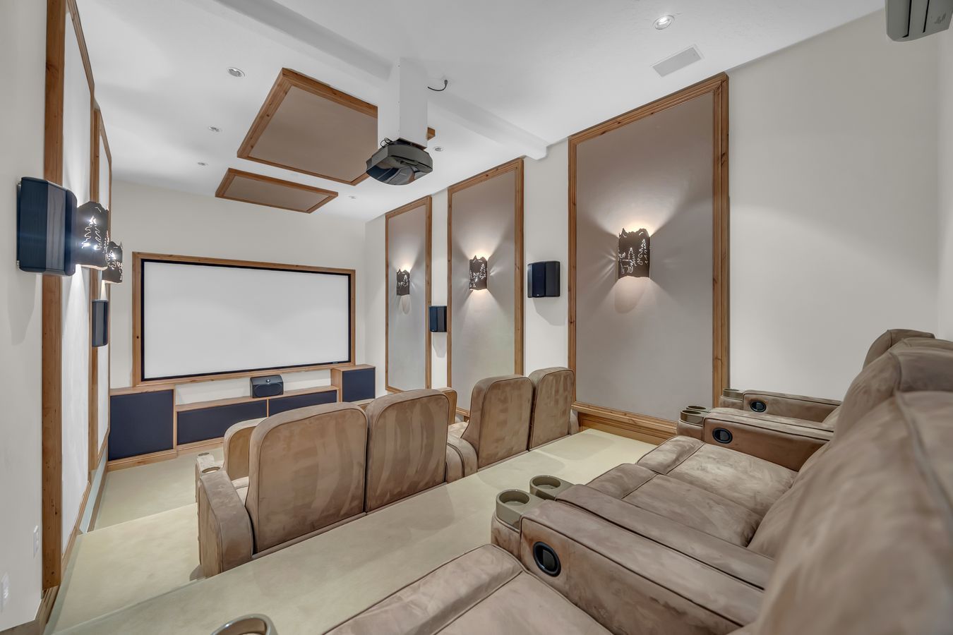 Dedicated media room featuring tiered seating, a large projection screen, built-in sound system, recessed lighting, and integrated wall sconces