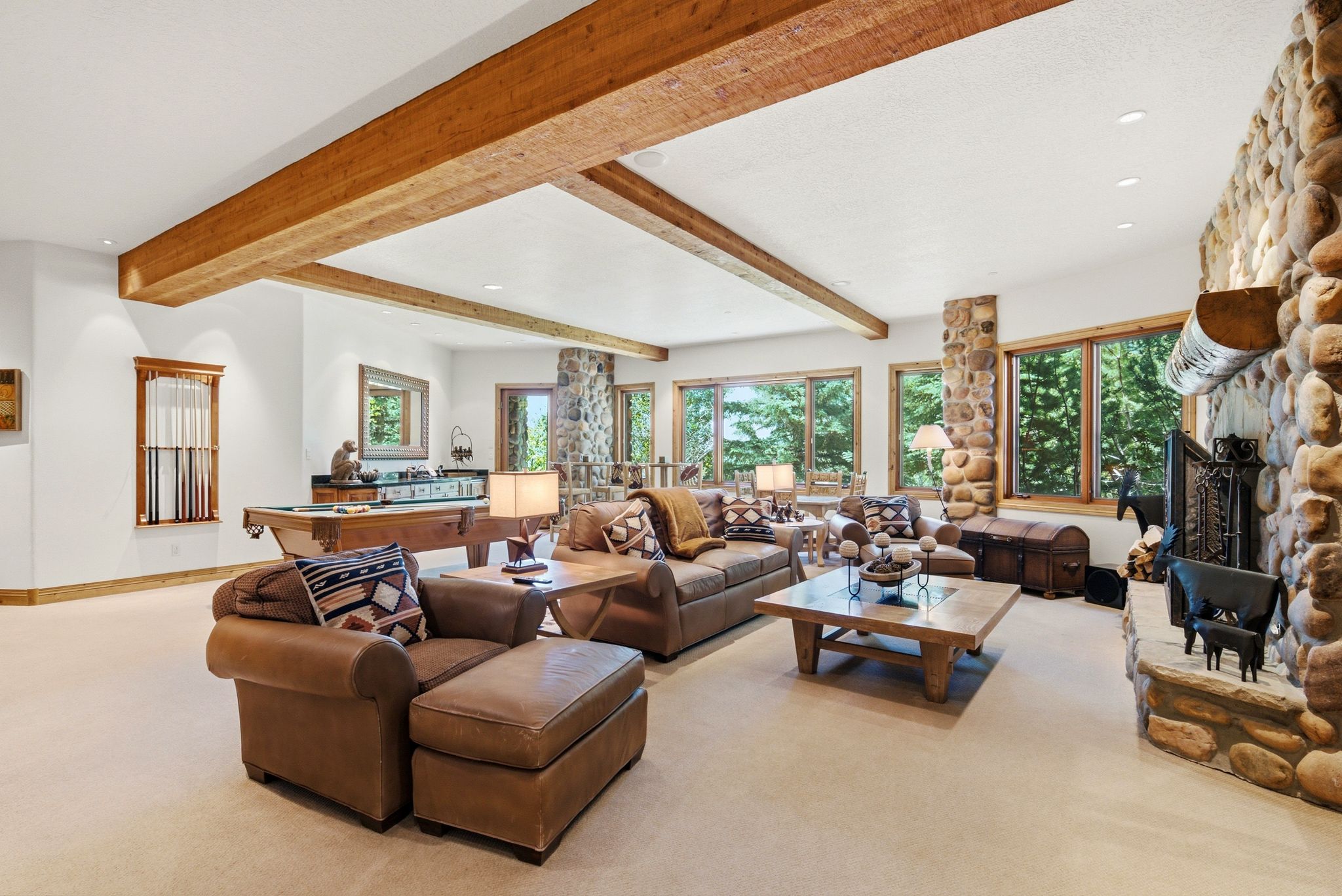 Spacious entertainment room featuring exposed wood beams, a stone-clad fireplace with a wood mantle, and a built-in wet bar