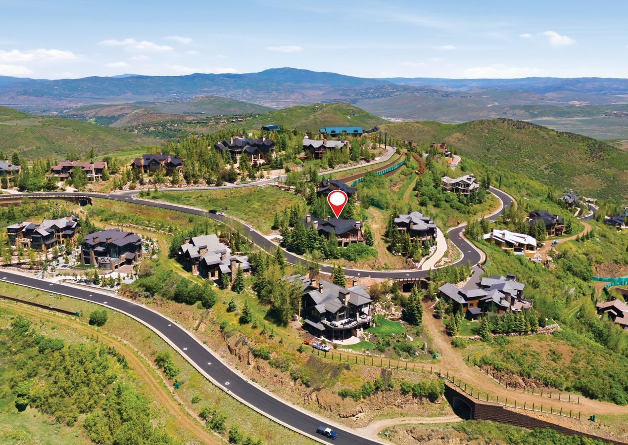 Hillside property with a multi-level structure, dark roof, and extensive surrounding greenery