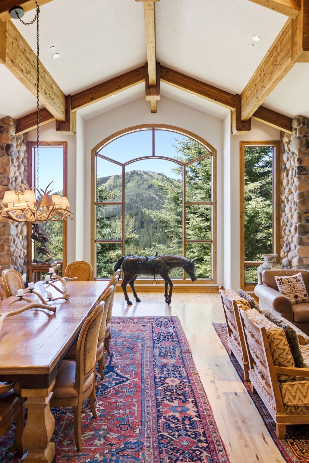 Vaulted ceiling with exposed wood beams, expansive arched window, stone accent wall, wood-finish flooring, and built-in lighting