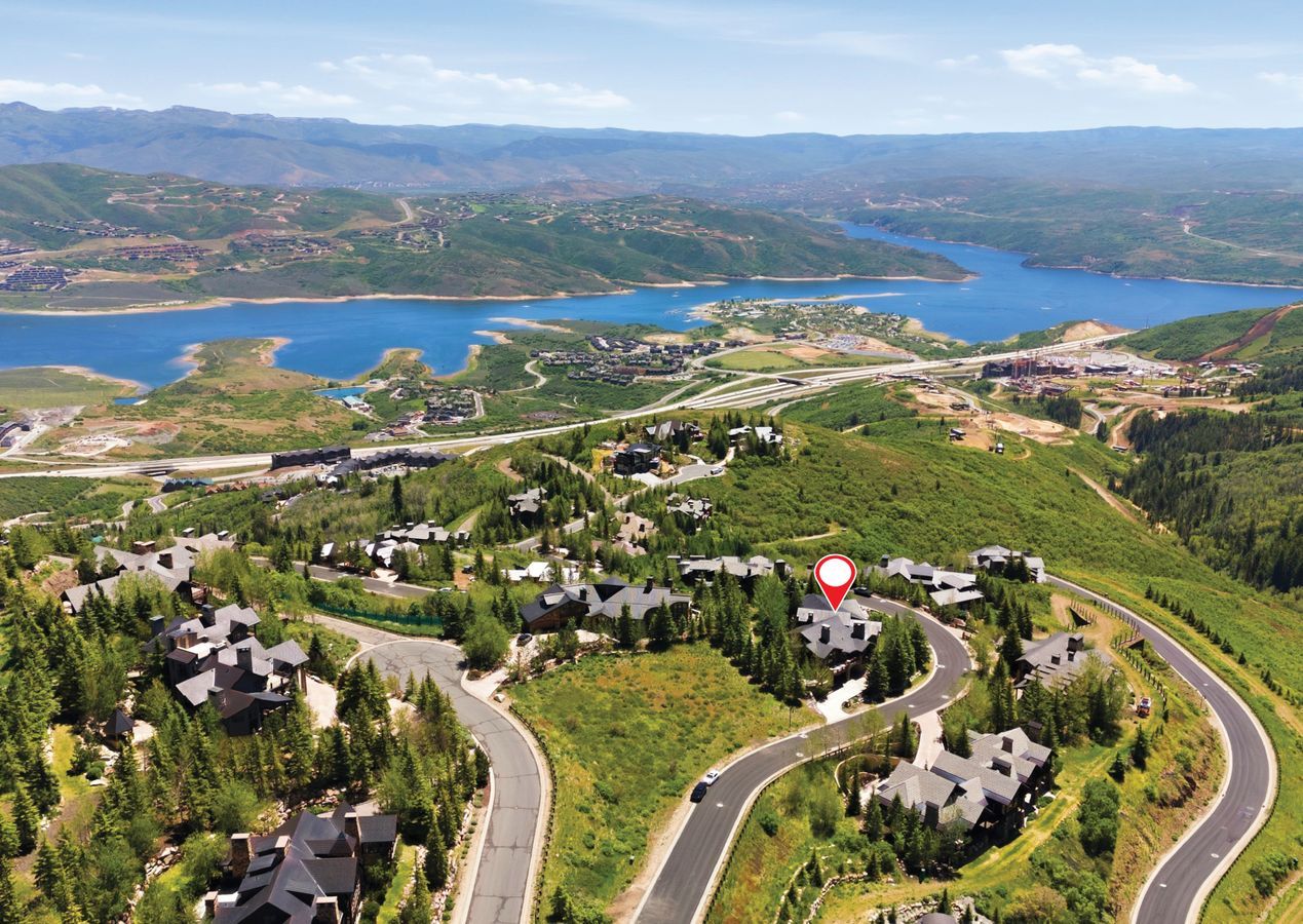 Expansive hillside property featuring a multi-level residence, dense natural landscaping, paved winding roadways, and a prominent distant lake
