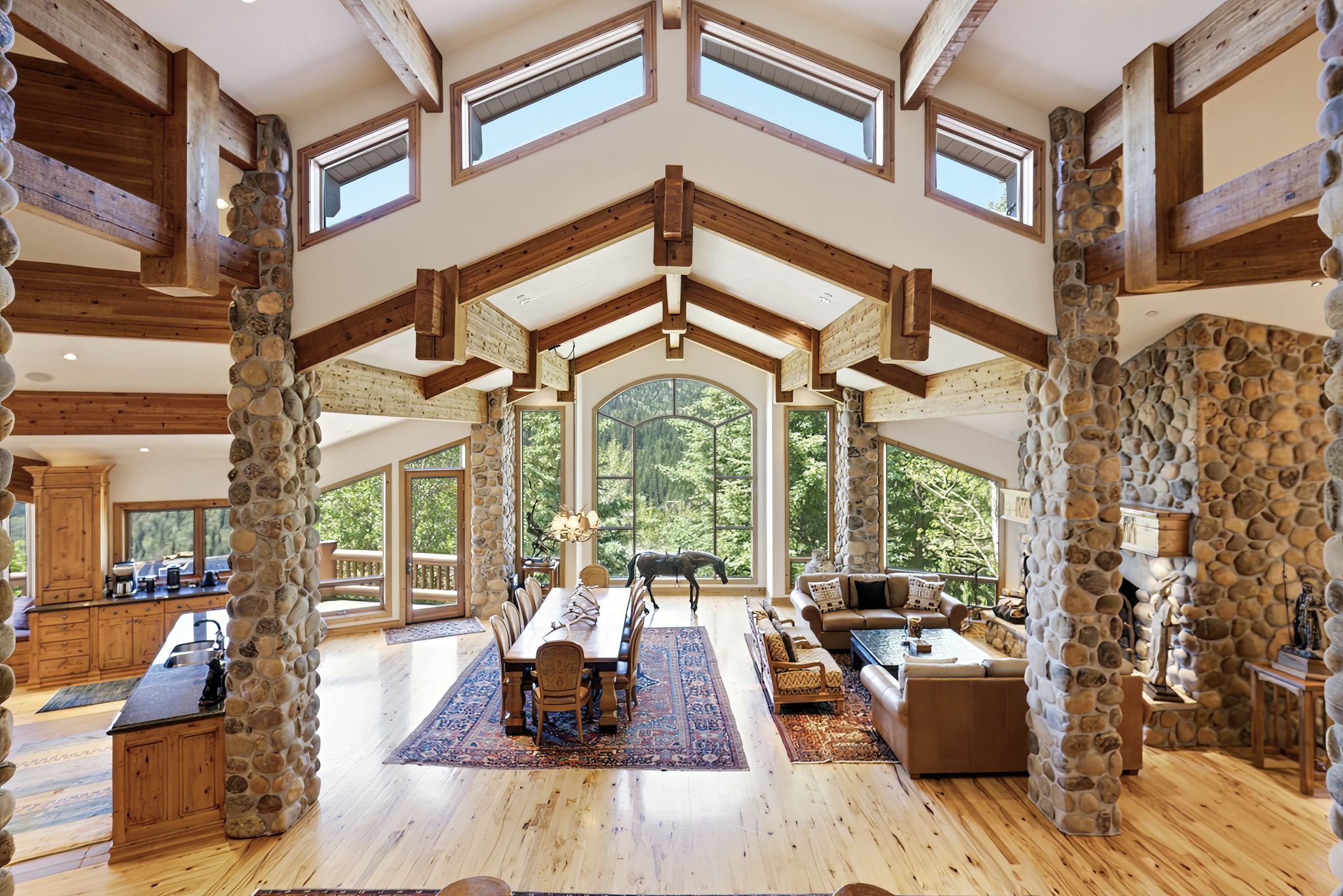 Grand living space featuring a vaulted ceiling with exposed wood beams, stone pillar accents, and light wood-finish flooring
