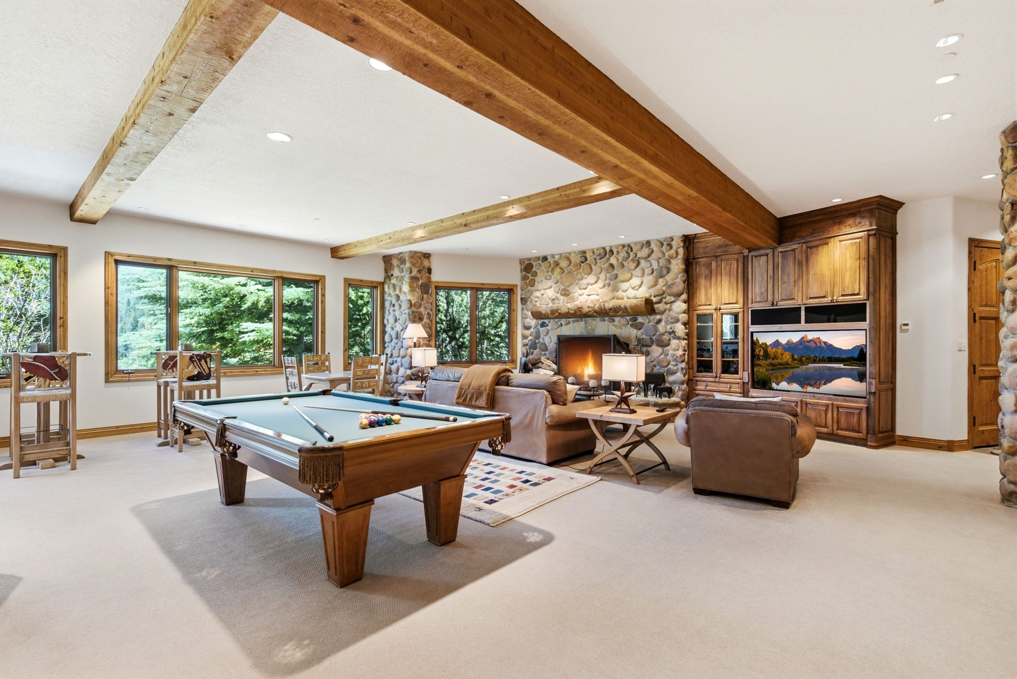 Spacious entertainment room featuring exposed wood ceiling beams, a stone-clad fireplace, and a built-in media center with wood cabinetry
