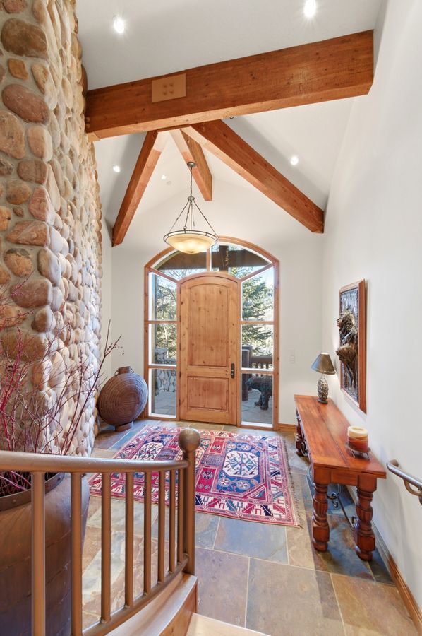 Grand entryway featuring a vaulted ceiling with exposed wood beams, a stone accent wall, and natural stone tile flooring