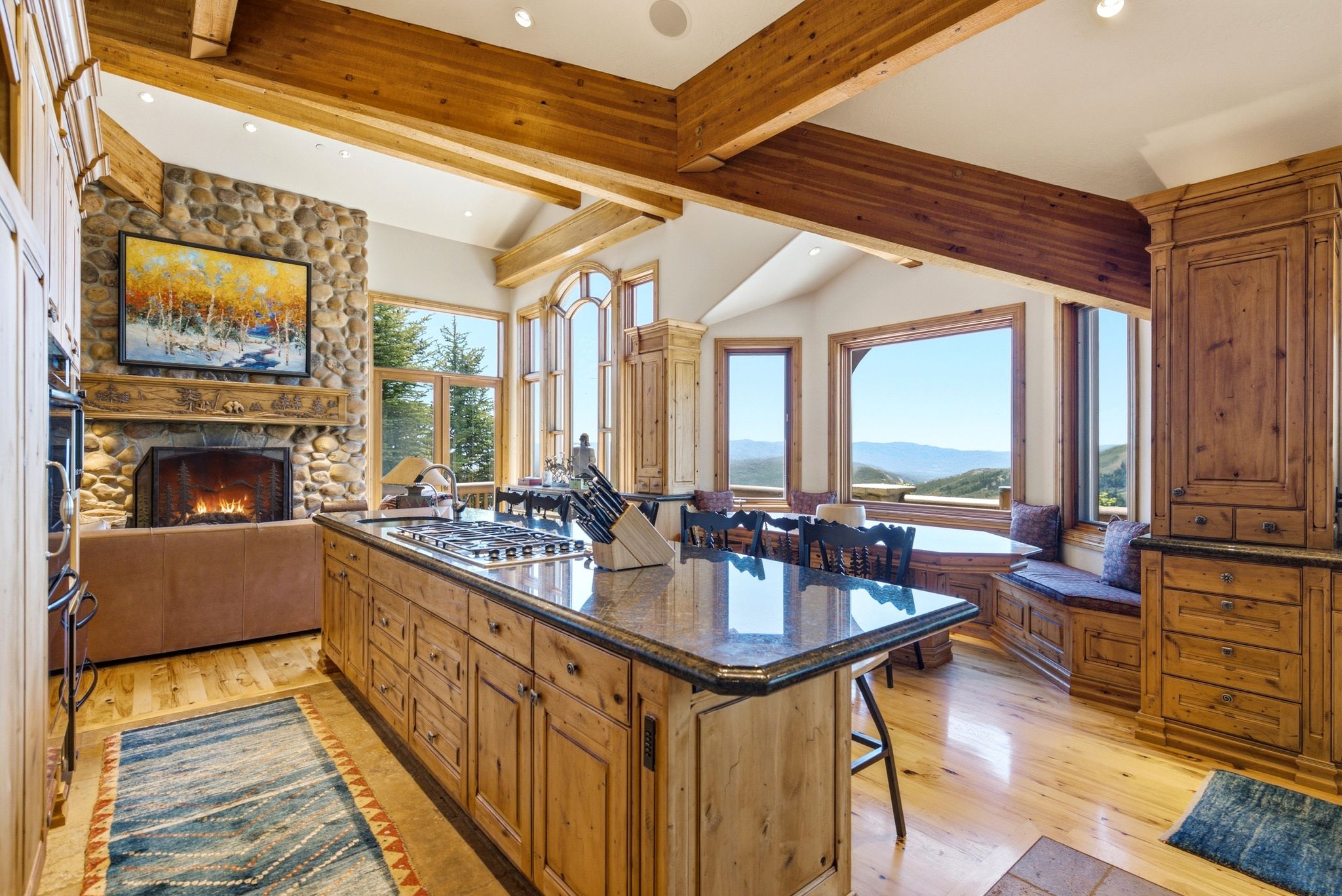 Kitchen featuring a center island, hardwood flooring, stone fireplace, exposed wood beams, and a dining area with built-in bench seating