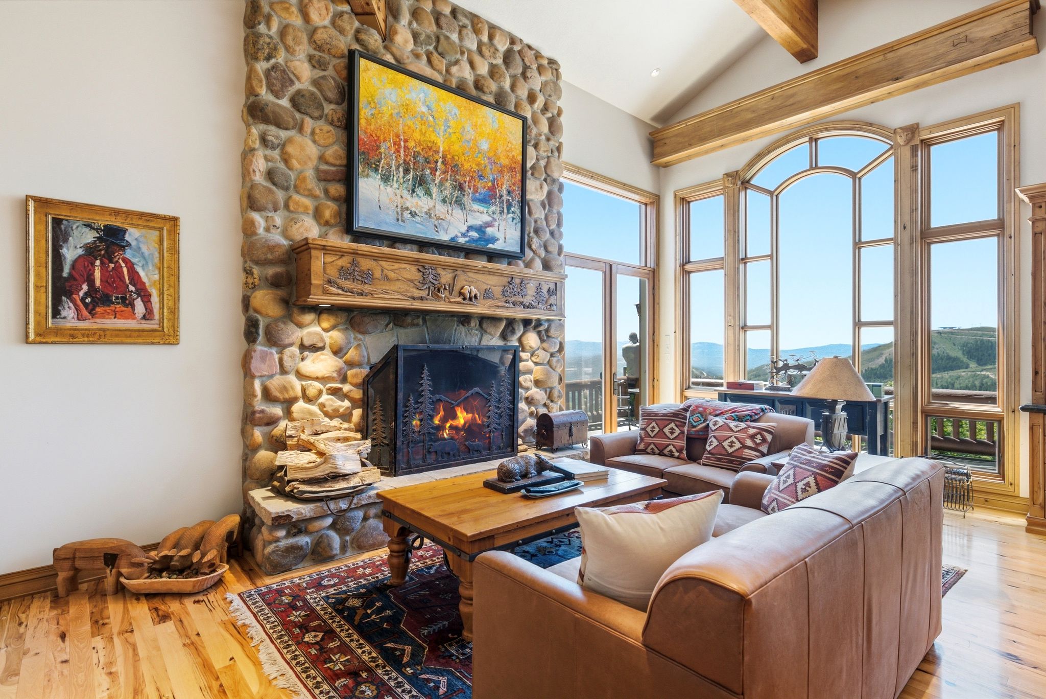Stone fireplace with a carved wood mantel, hardwood flooring, and vaulted ceilings with exposed wood beams