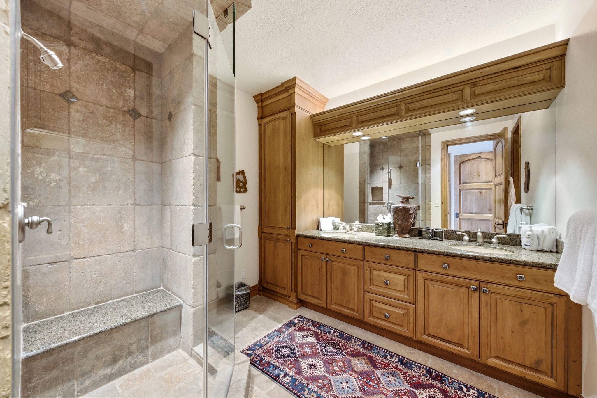 Glass-enclosed shower with stone tile walls and integrated bench seating