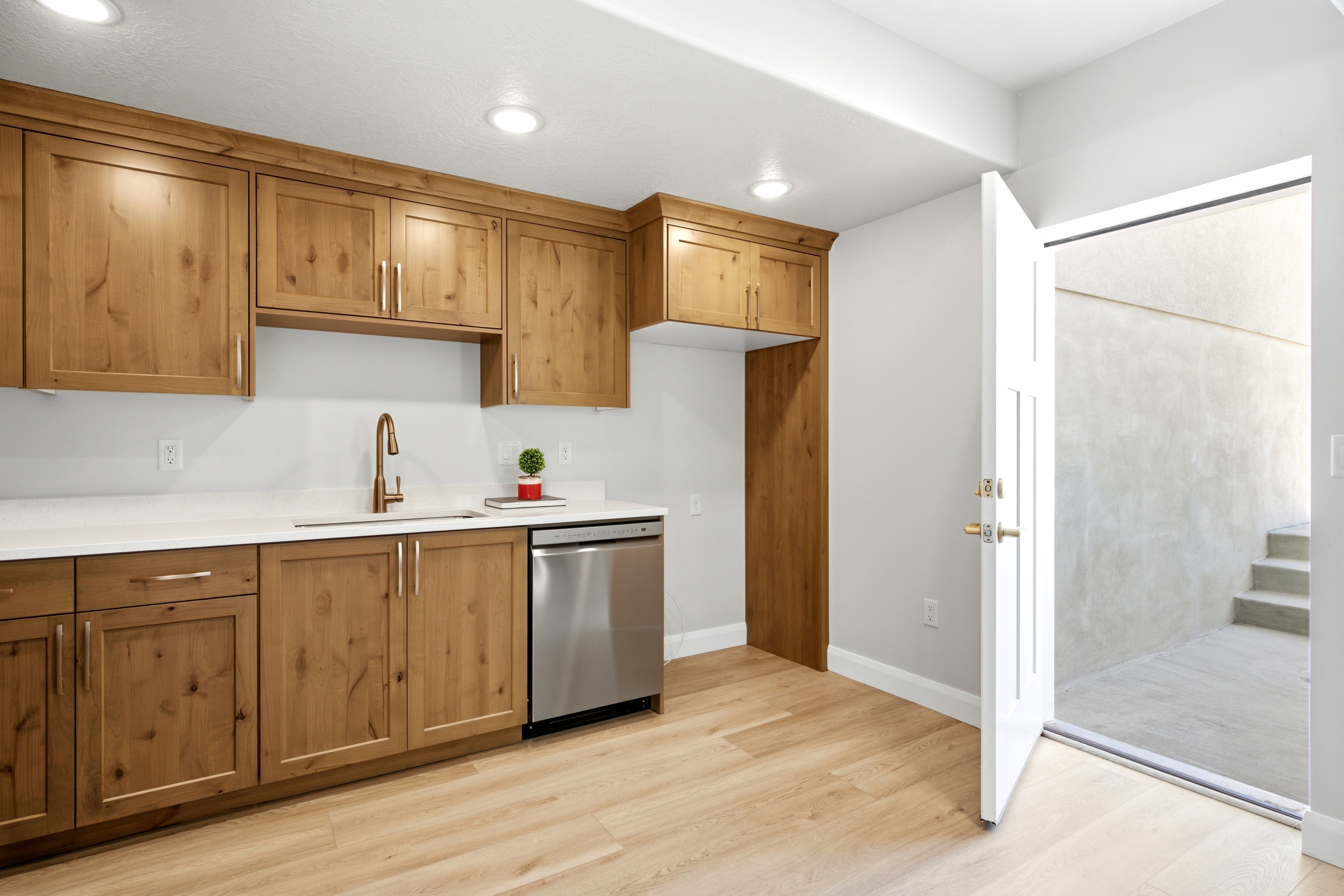 Kitchenette featuring wood-finish cabinetry, white countertops, a single basin sink with a bronze-finish faucet, and a stainless steel dishwasher