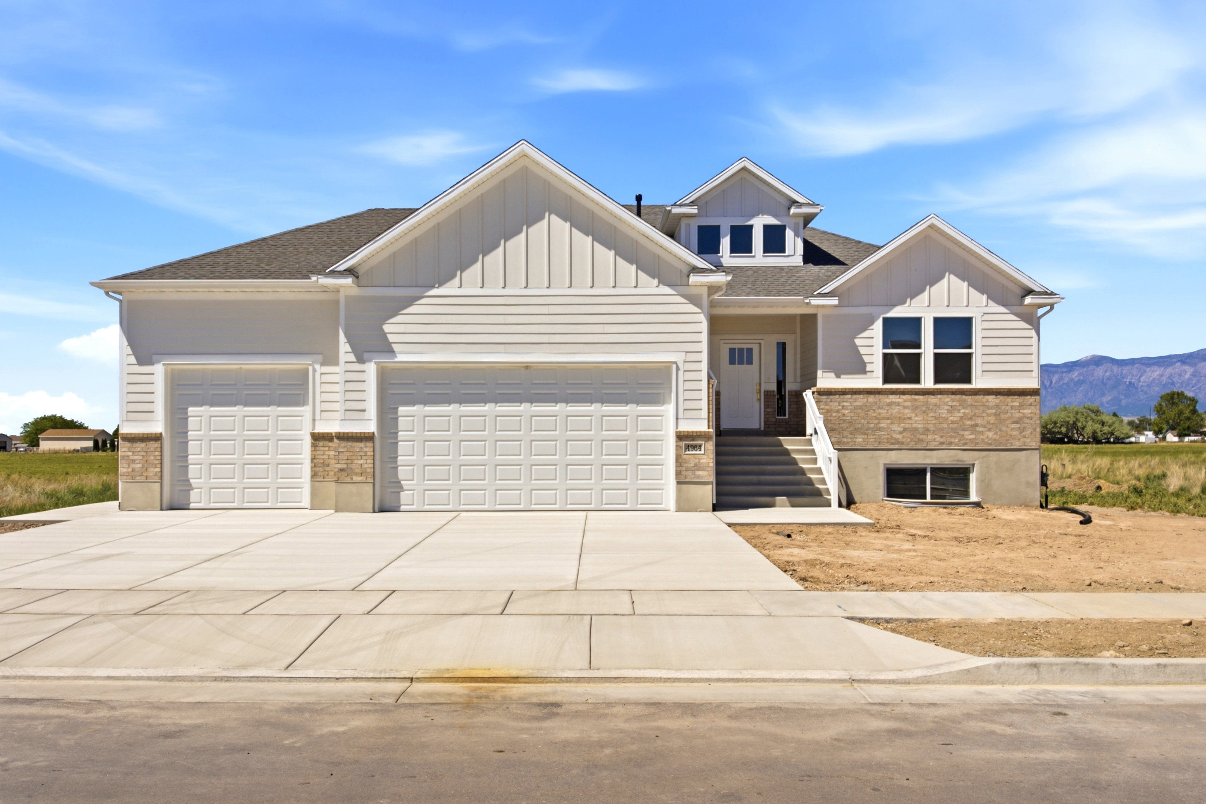 Contemporary two-story residence featuring a two-car garage, white siding, and a stone veneer foundation