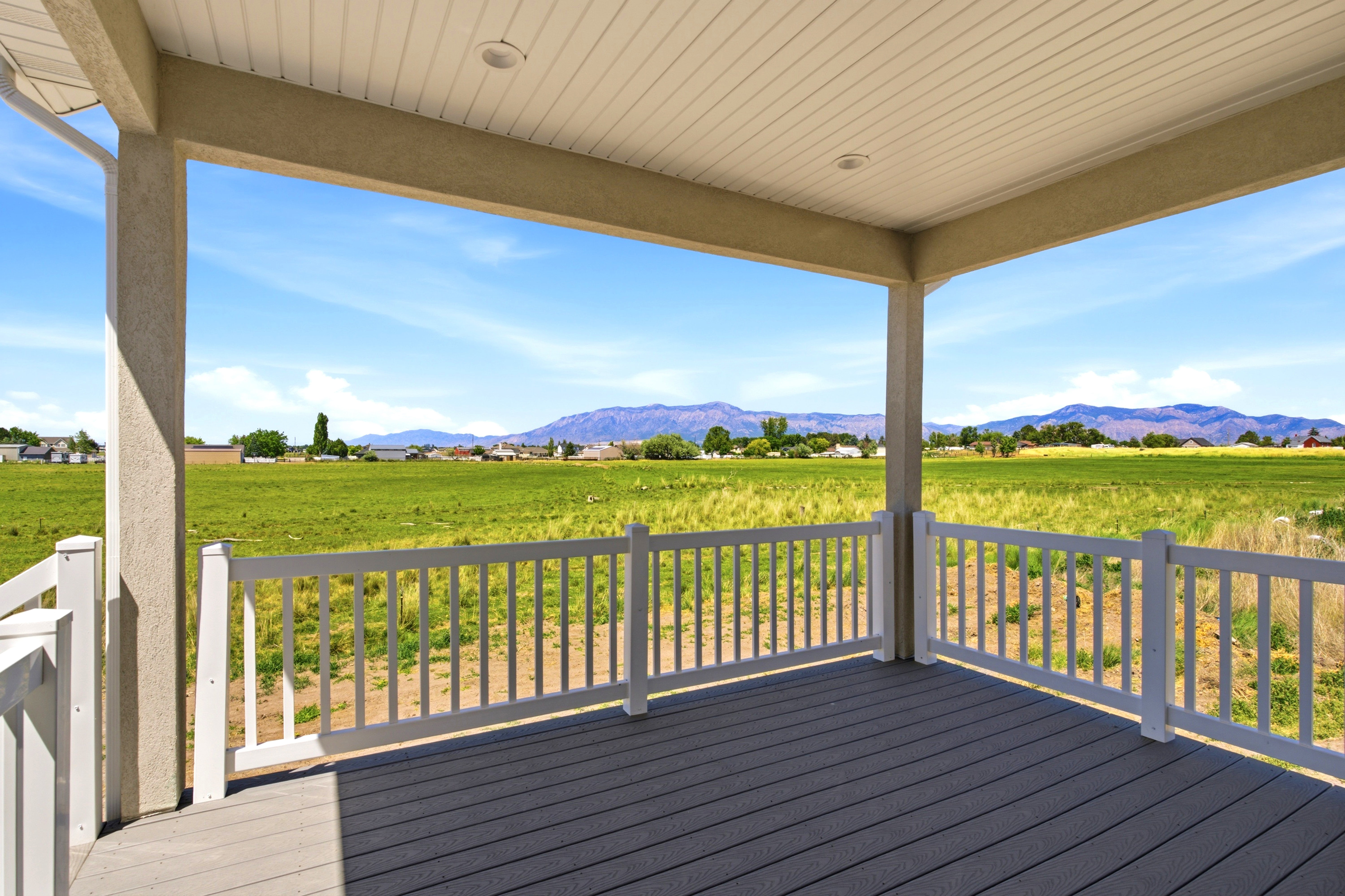 Covered patio featuring composite decking, white railing, recessed lighting, and expansive green field scenery with distant mountains