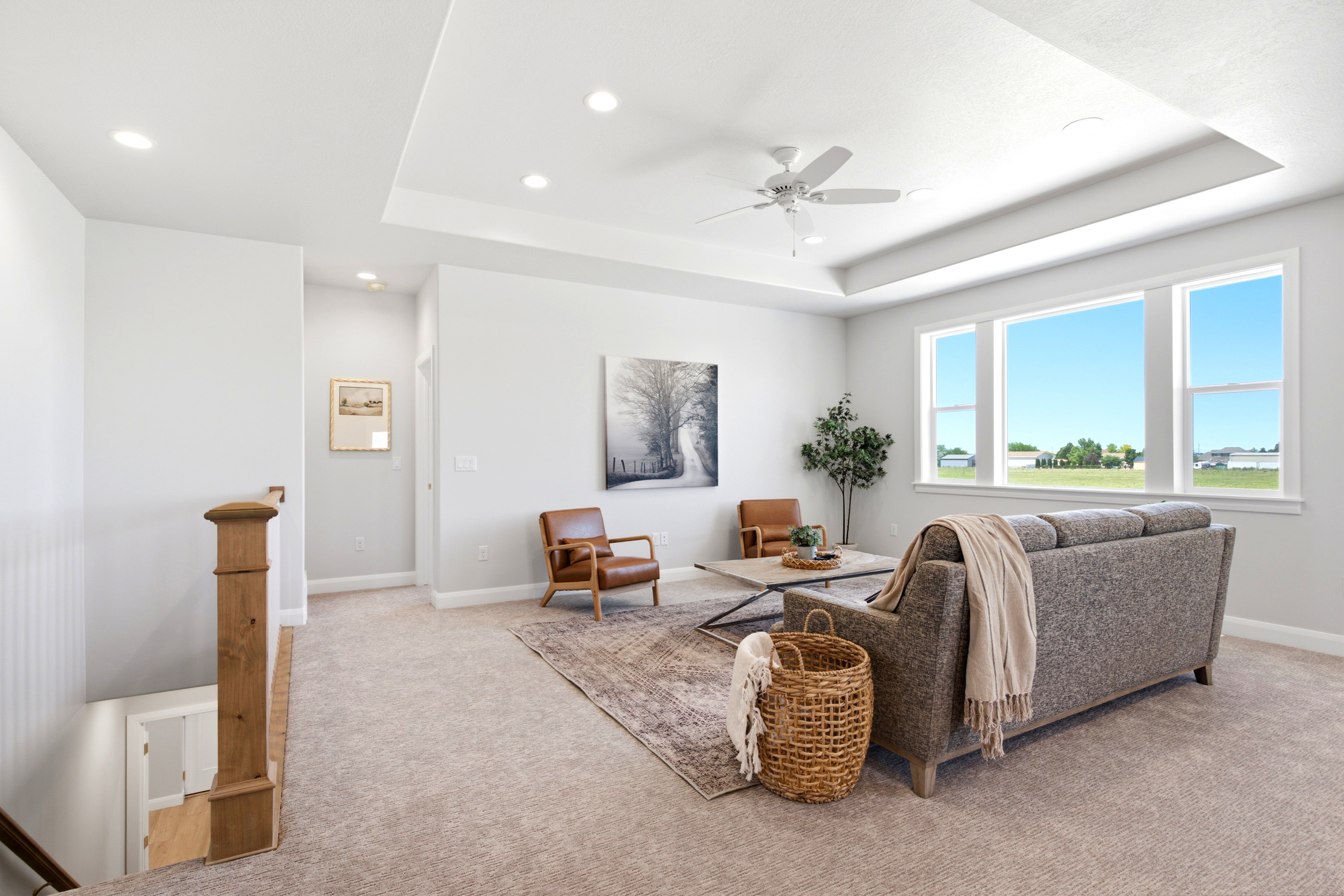 Expansive living area with a tray ceiling and recessed lighting, featuring large windows, a ceiling fan, and carpet flooring