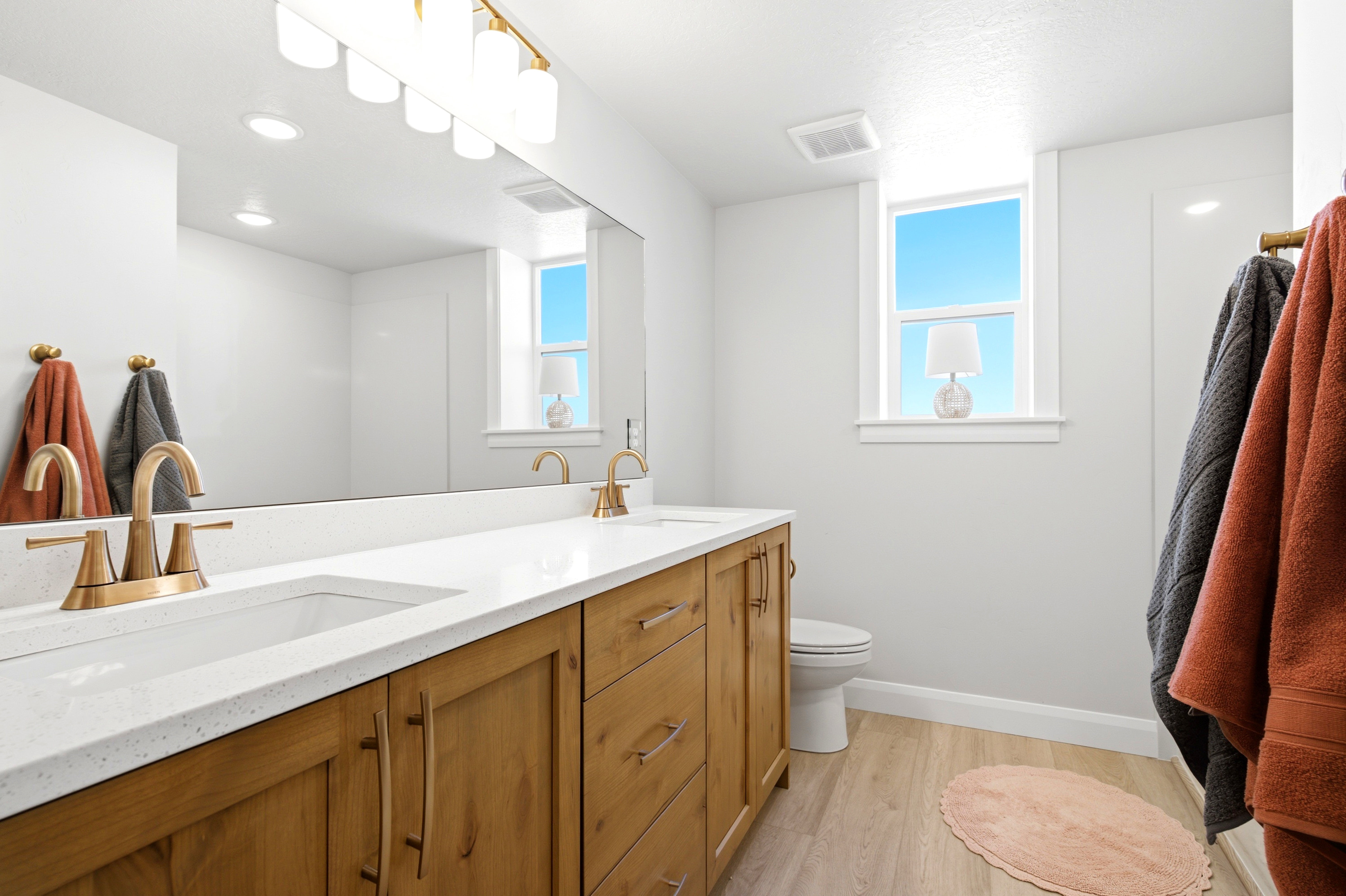 Bathroom featuring a dual vanity with light wood cabinetry, white countertops, and brass fixtures