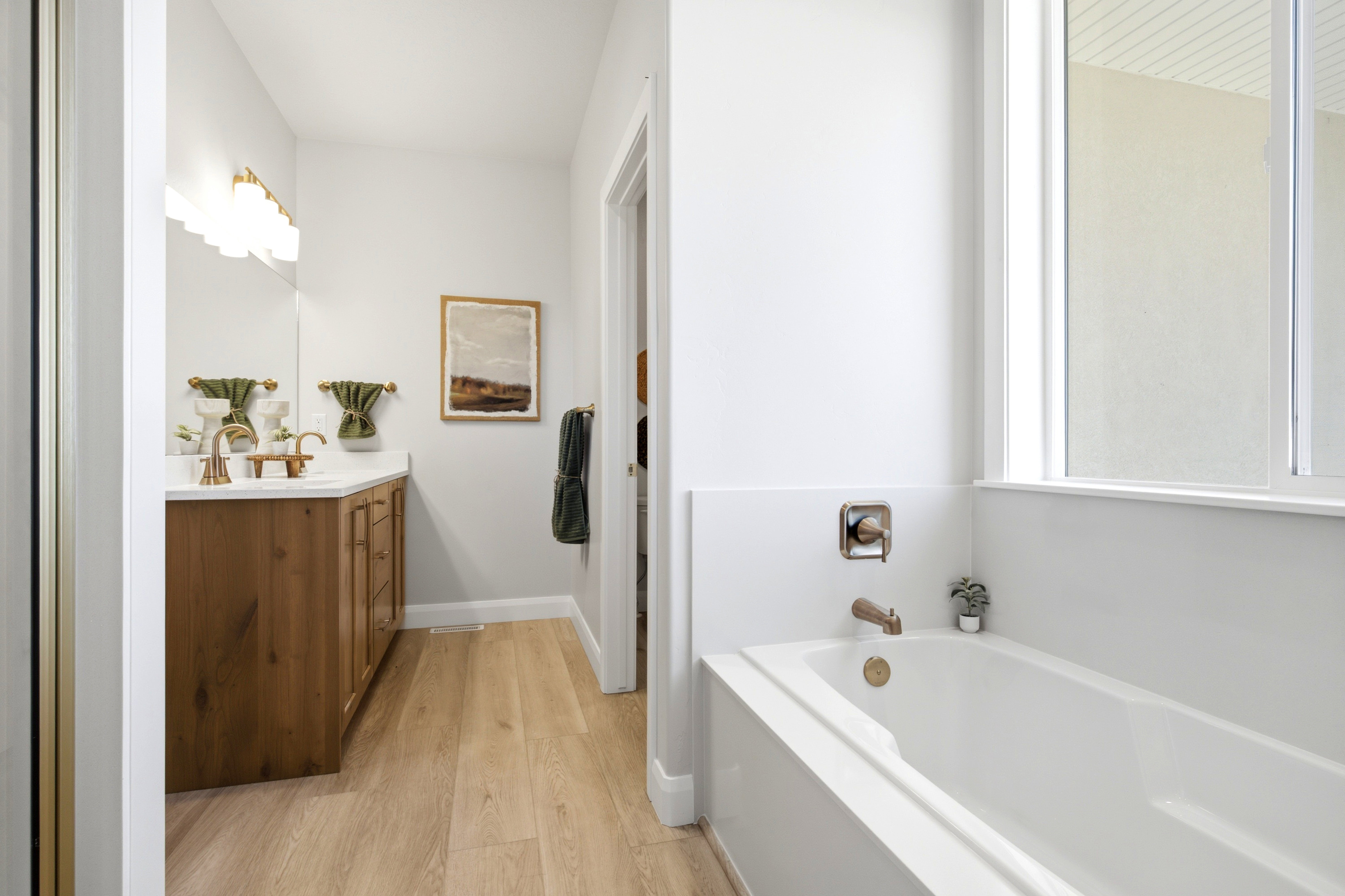 Modern bathroom featuring a soaking tub with brass fixtures and a natural wood-finish vanity with dual sinks