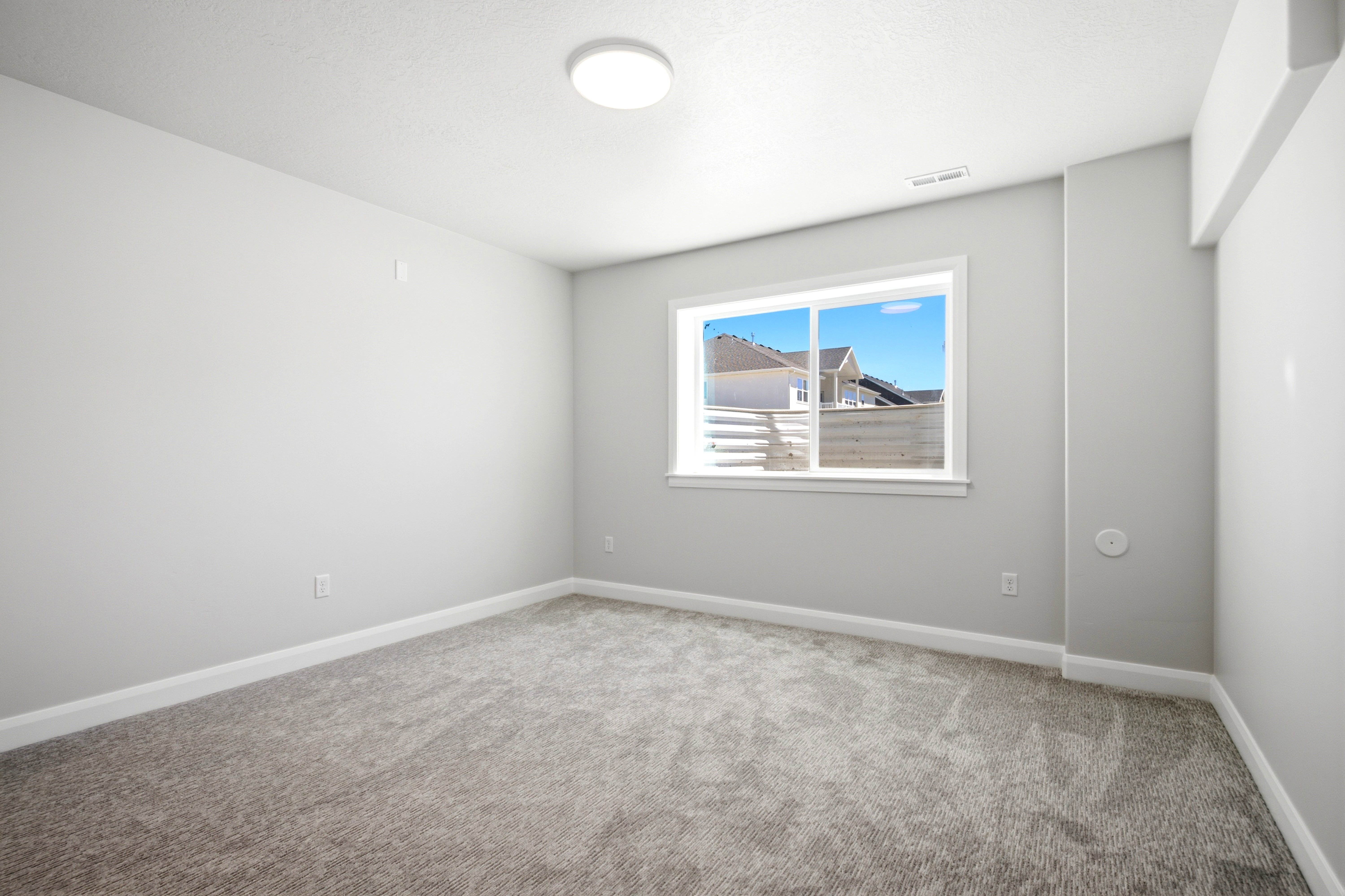 Neutral toned room featuring a single window, overhead flush-mount lighting, light gray carpeting, and white baseboards