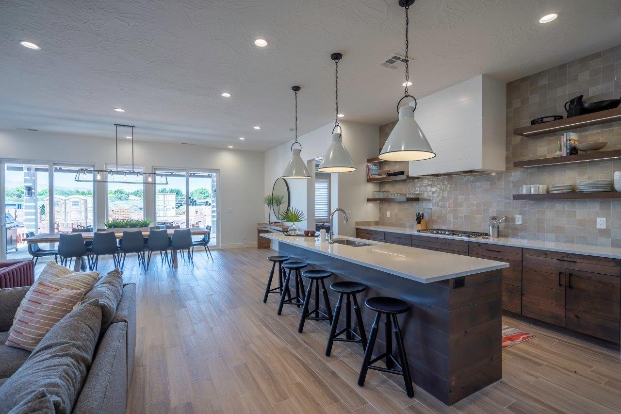 Open-concept interior featuring light wood-finish flooring, a kitchen island with seating, dark wood cabinetry, and a tile backsplash