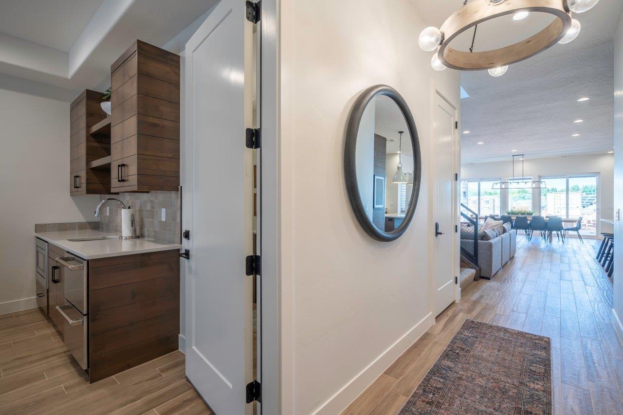 Entryway featuring wood-finish flooring, a contemporary overhead light fixture, and a built-in wet bar with wood cabinetry, a stainless steel under-counter refrigerator, and a coordinating sink with a pull-down faucet