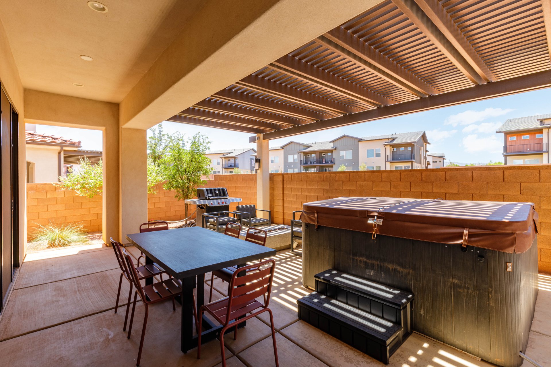 Covered patio featuring a slatted pergola, paver flooring, and a built-in spa with steps