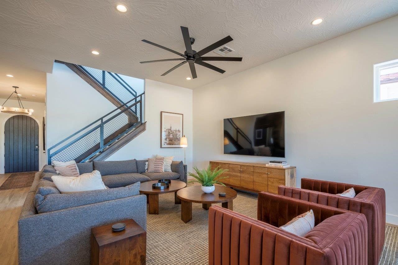 Open living area featuring a prominent staircase with industrial-style metal and wood railings, wood-finish flooring, recessed lighting, and a large ceiling fan