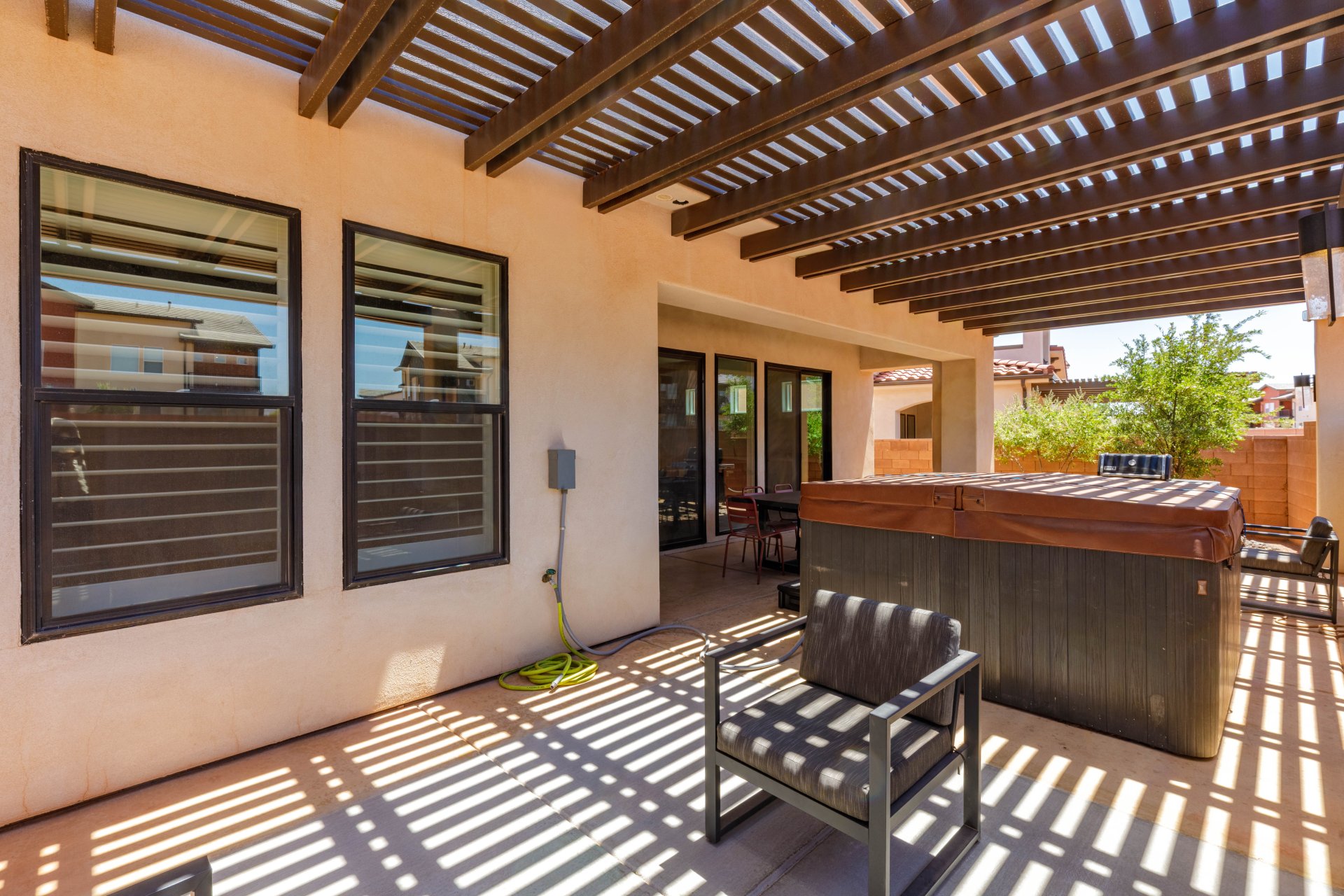 Patio area featuring a slatted wood pergola, stucco exterior, and a built-in hot tub with cover
