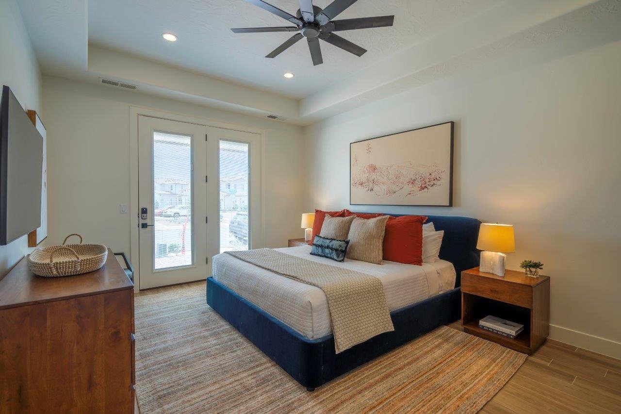 Bedroom featuring double glass-paneled doors, a tray ceiling with recessed lighting, a ceiling fan, wood-finish flooring, and a large area rug