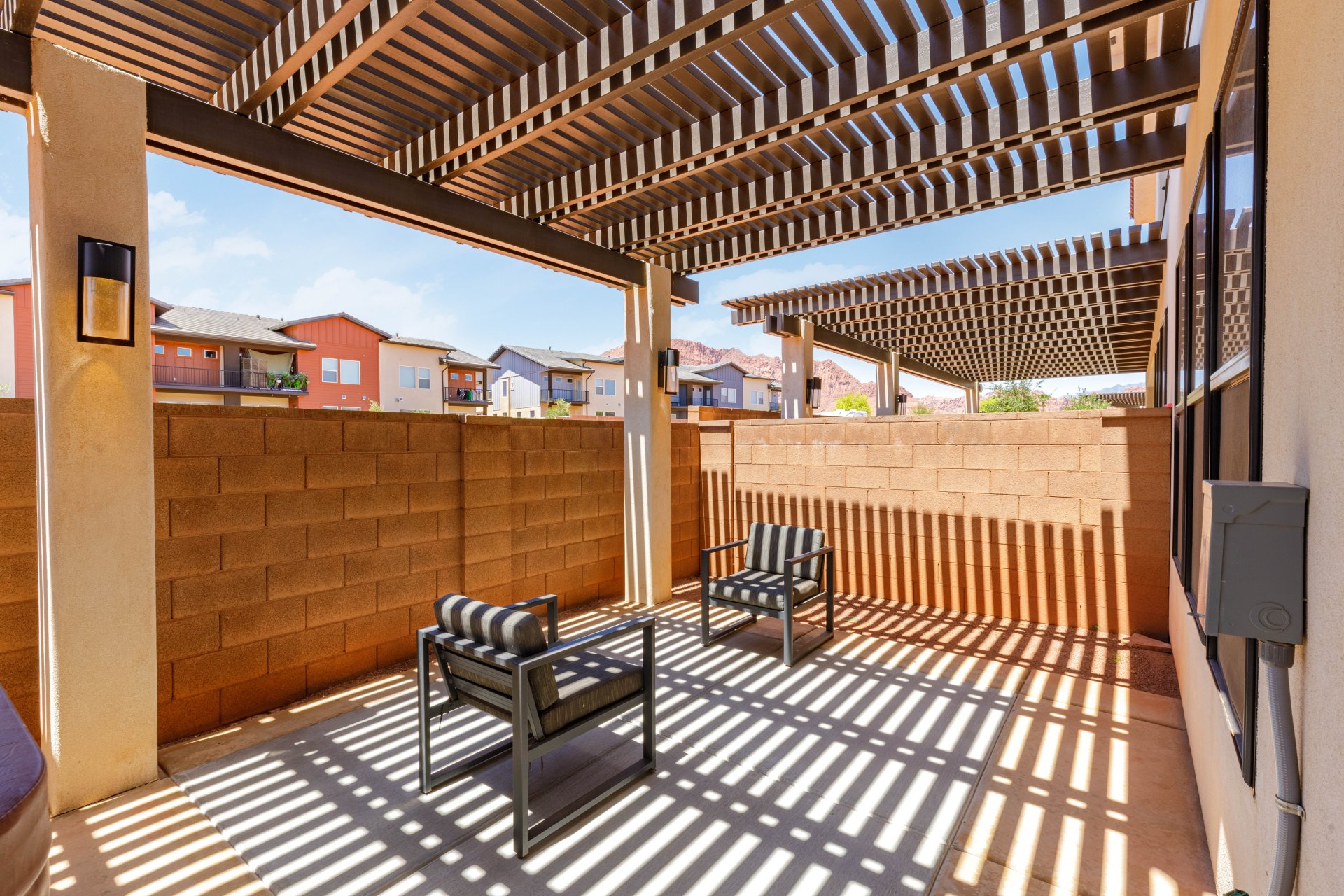 Covered patio with a slatted pergola ceiling, concrete flooring, and a block wall perimeter