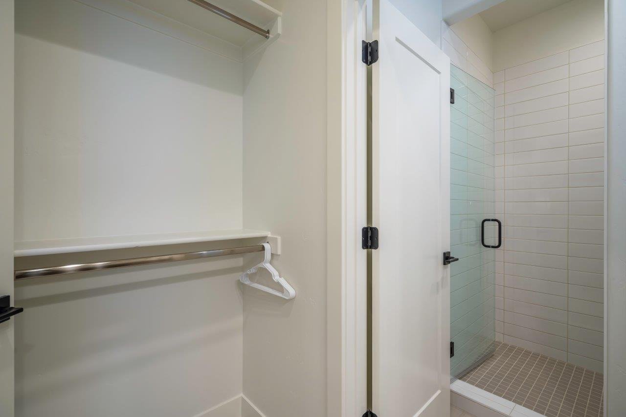 Bright white closet with dual chrome hanging rods, accompanied by a glass-enclosed shower featuring subway tile surround and a tiled floor