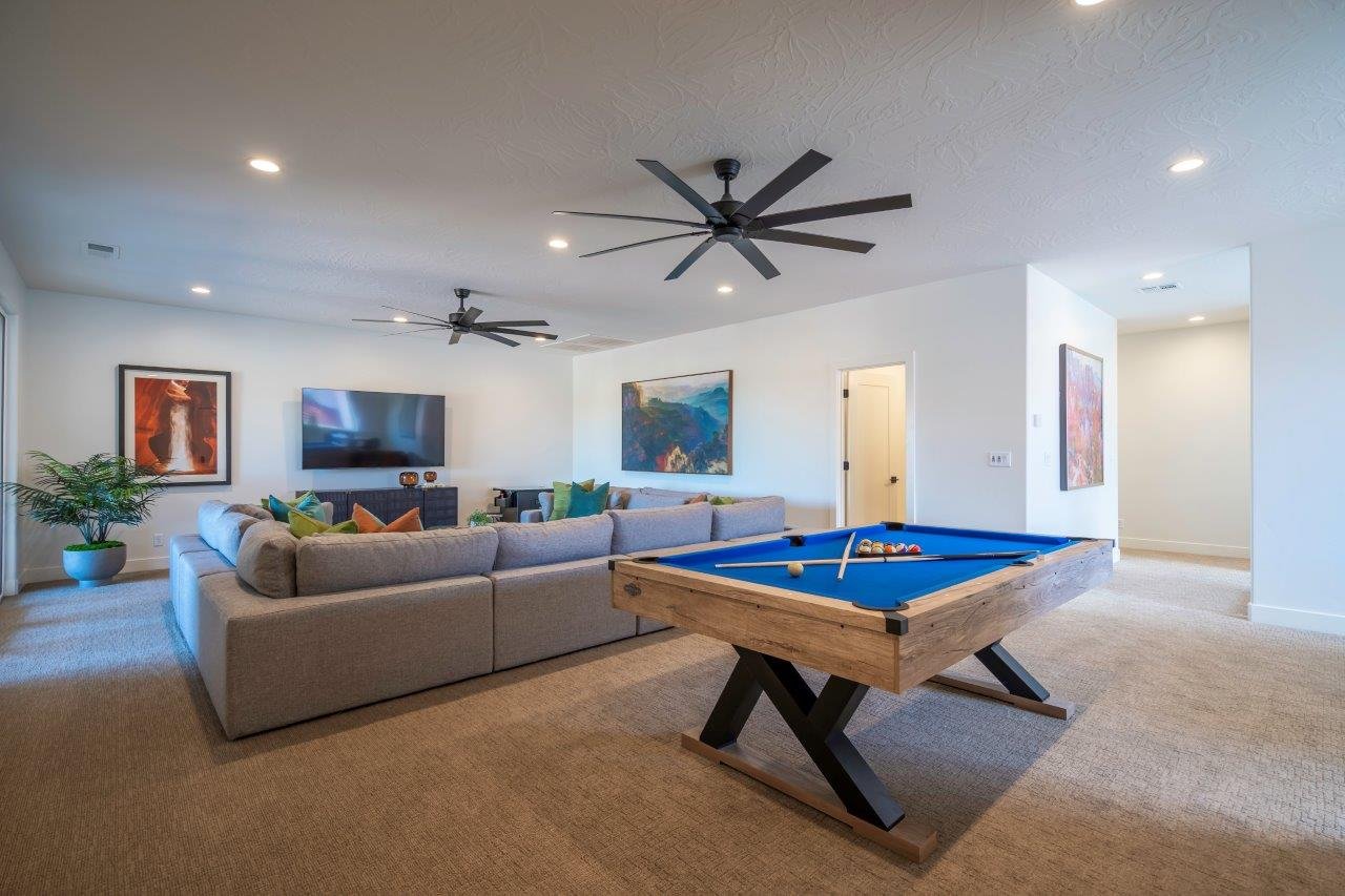 Spacious recreation room featuring a blue felt pool table, wall-mounted television, and two black ceiling fans