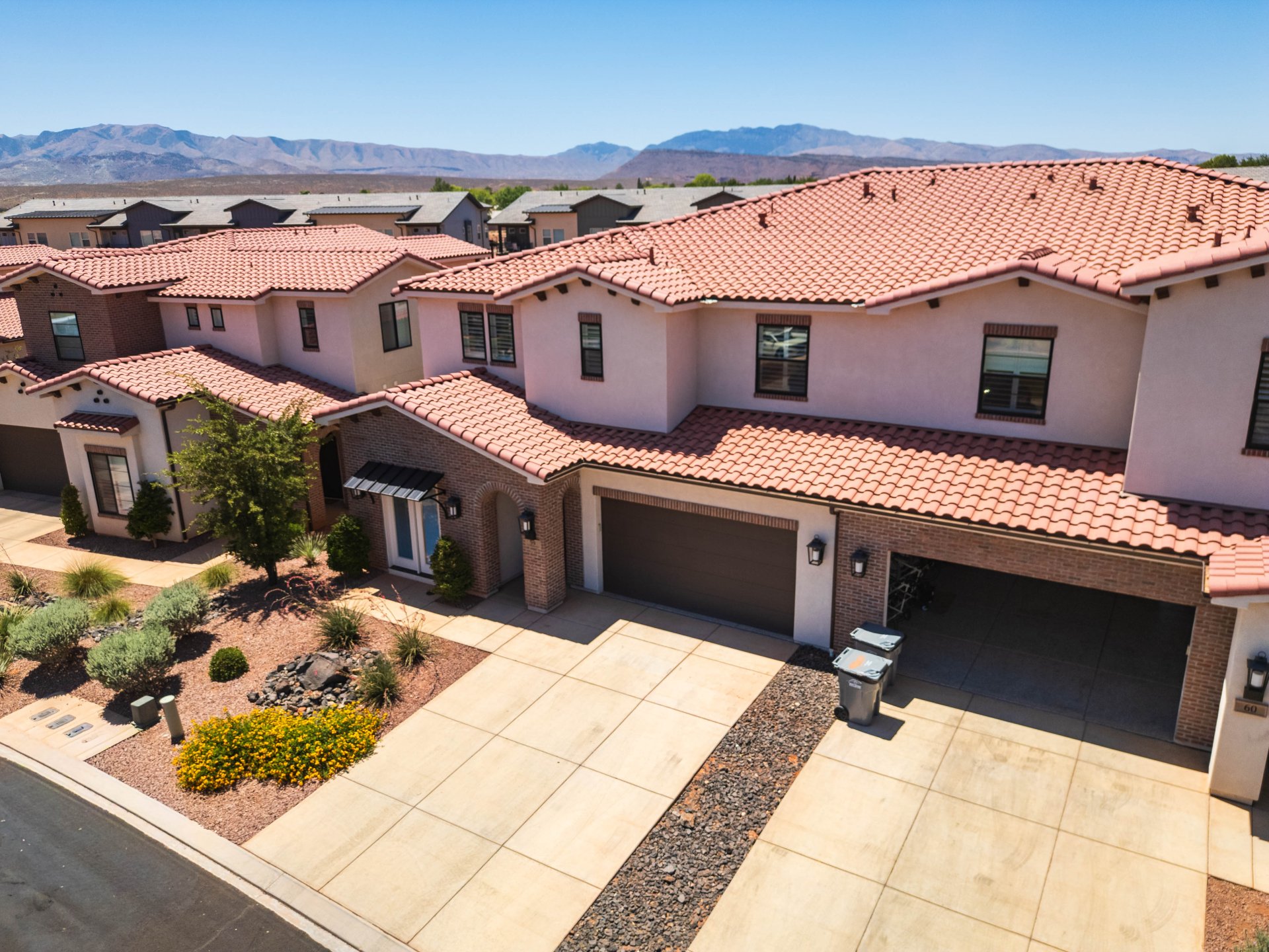 Mediterranean-style exterior featuring a red tile roof, stucco facade, brick accents, and attached garages