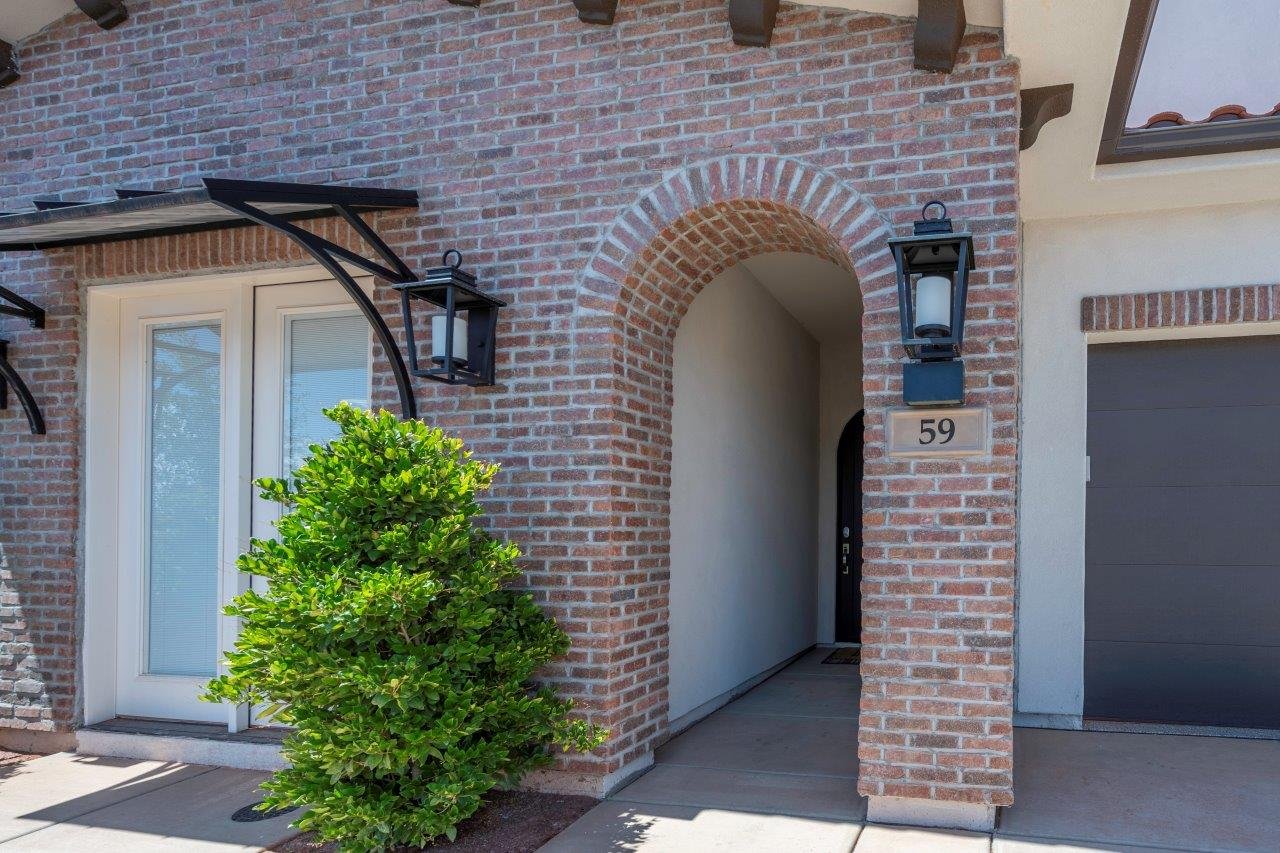 Brick exterior featuring a recessed entry archway, a covered entryway with a black metal awning, twin glass-paneled entry doors, and a dark-toned garage door