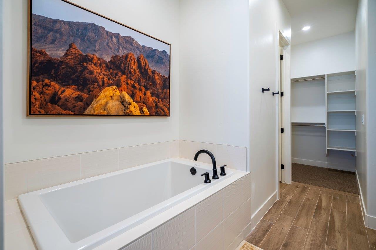 Built-in soaking tub with matte black fixtures, white tile surround, and wood-finish flooring