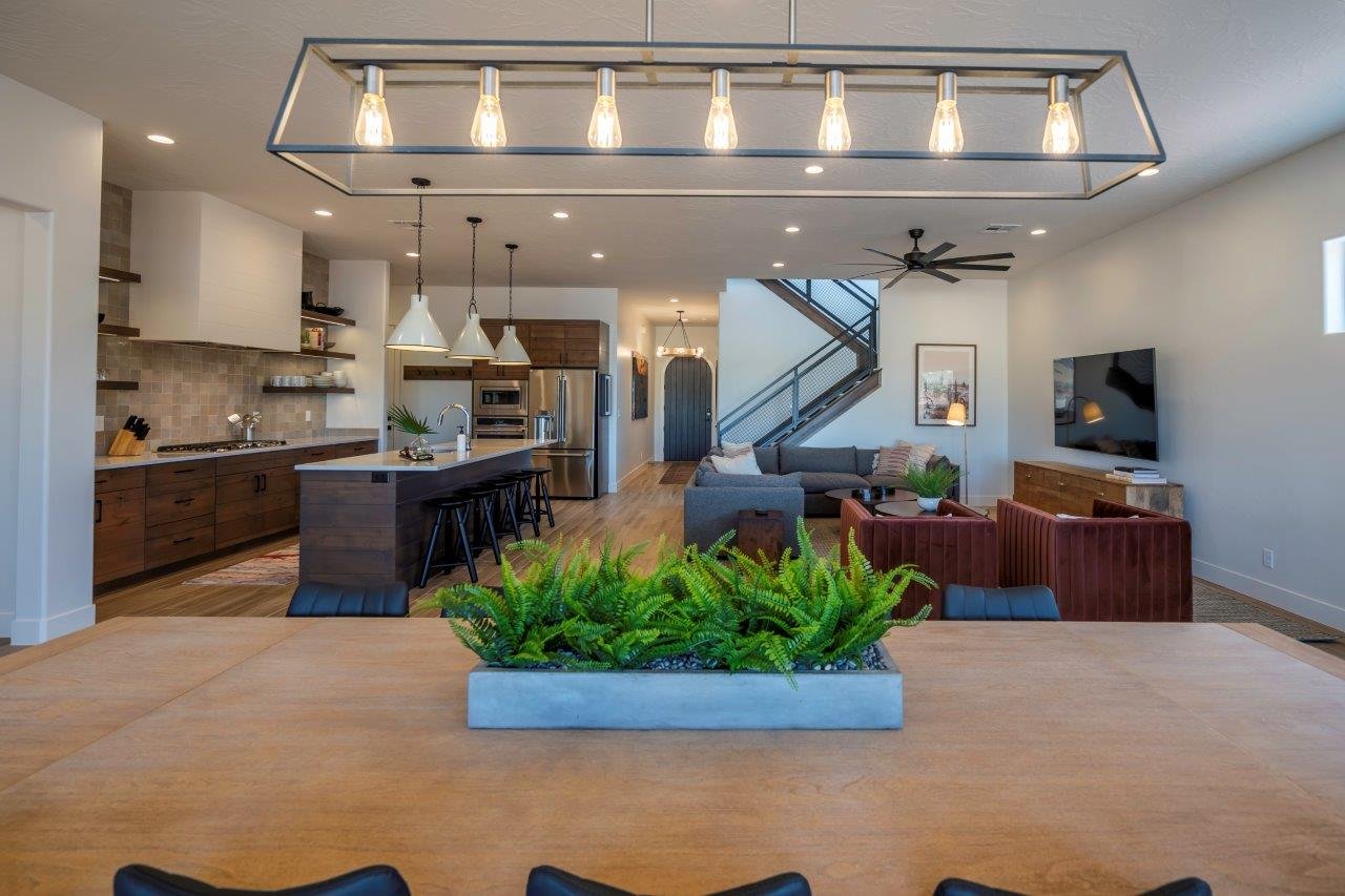 Open-concept living space featuring a modern kitchen with wood cabinetry, a large island with pendant lighting, a built-in range hood, and open shelving