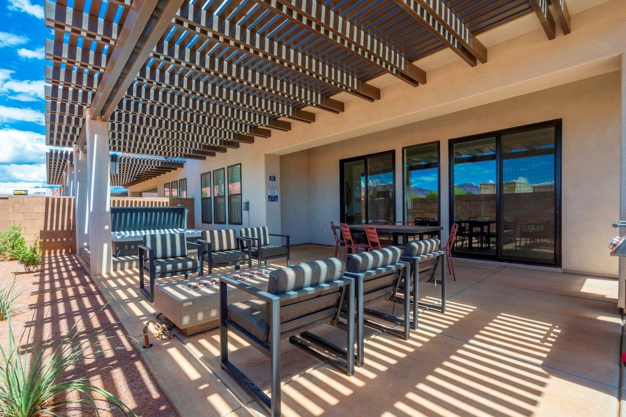 Expansive covered patio featuring a slatted pergola, concrete flooring, exterior stucco finish, and multiple glass sliding doors