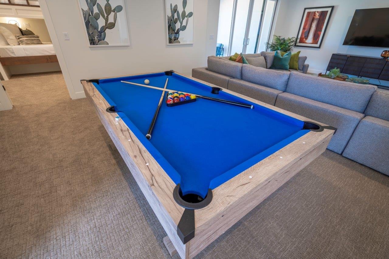 Recreation room featuring a wood-finish billiards table with blue felt, neutral carpet flooring, and a large sectional seating area