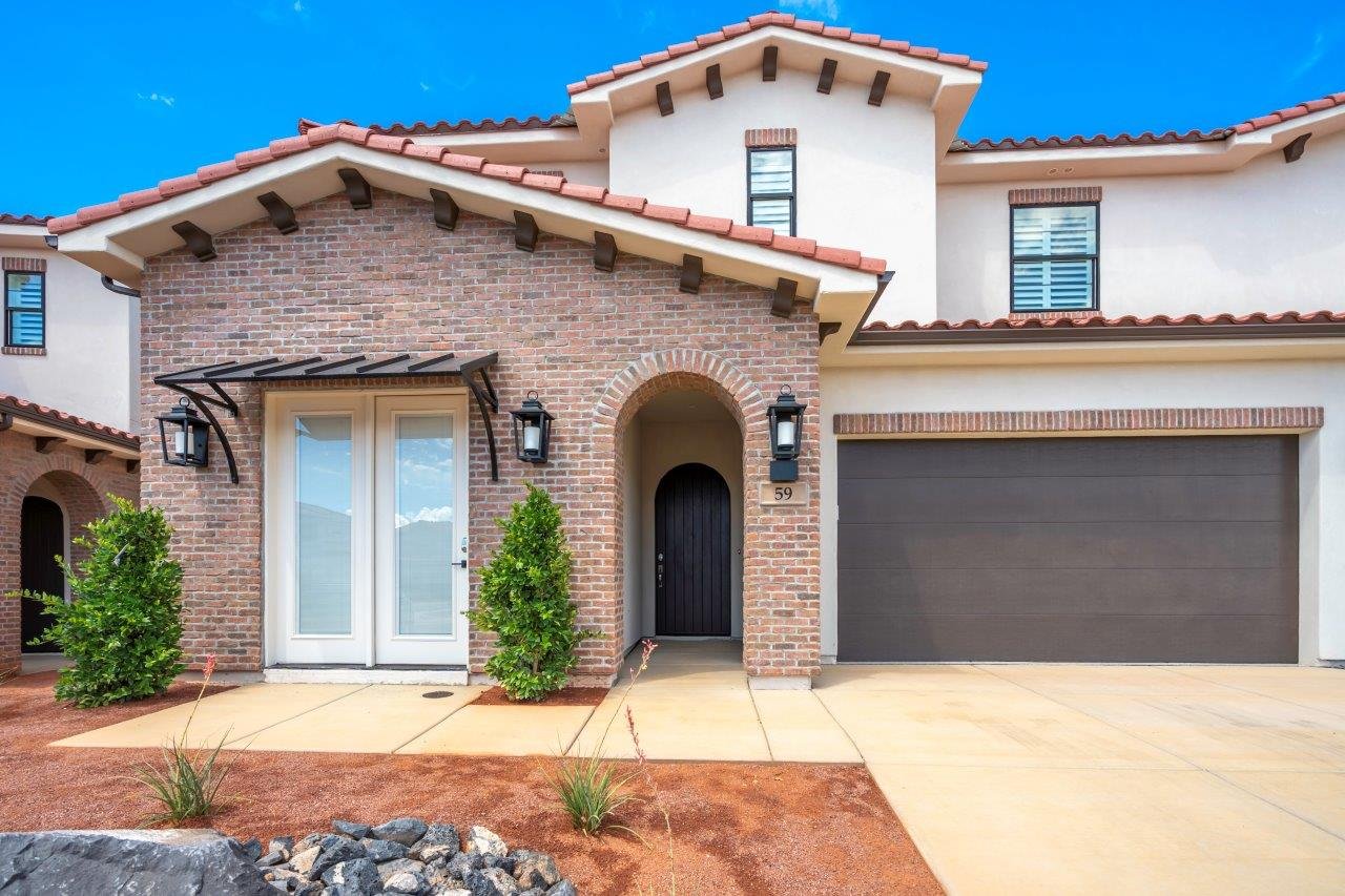 Mediterranean-style exterior featuring a clay tile roof, brick facade accents, arched entry, a dark wood front door, and a two-car garage
