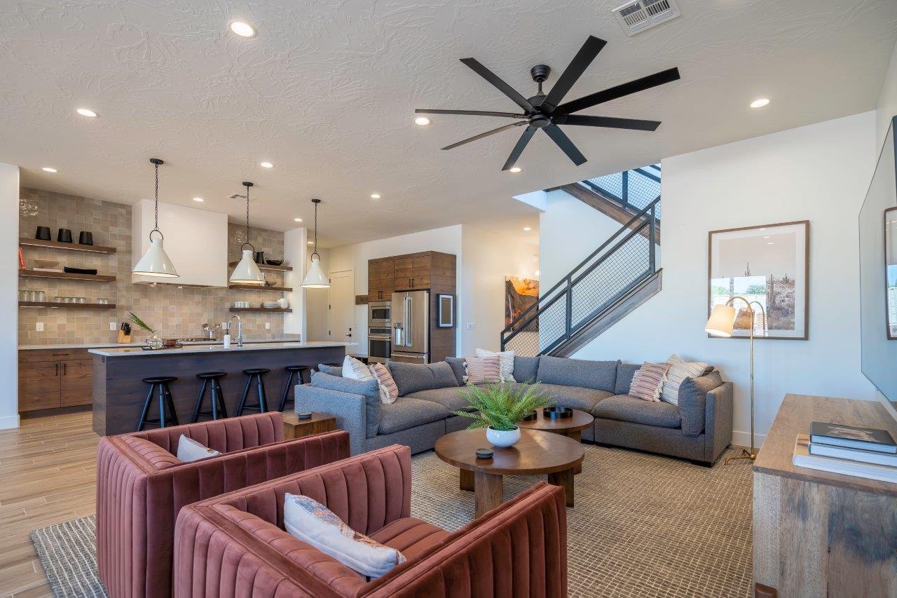 Open-concept living space featuring a modern kitchen with island seating, wood-finish flooring, a contemporary ceiling fan, and a staircase with metal railings