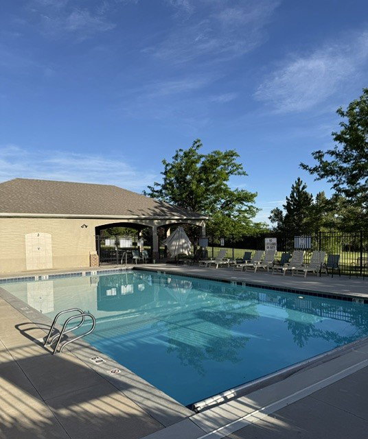 Community swimming pool with an integrated spa, surrounded by a concrete deck and a black metal fence