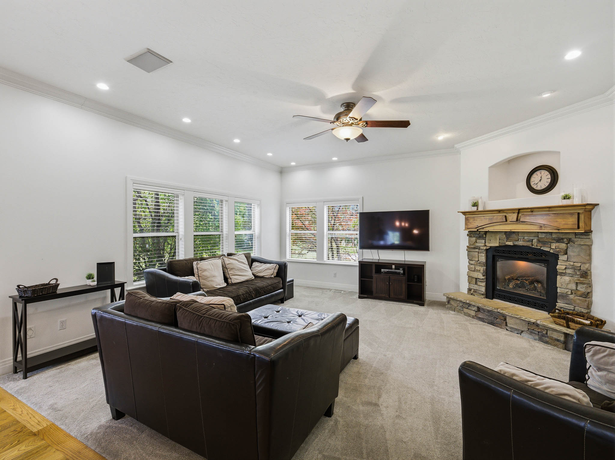 Living area featuring a stone fireplace with a wood mantel, crown molding, recessed lighting, a ceiling fan, and multiple windows
