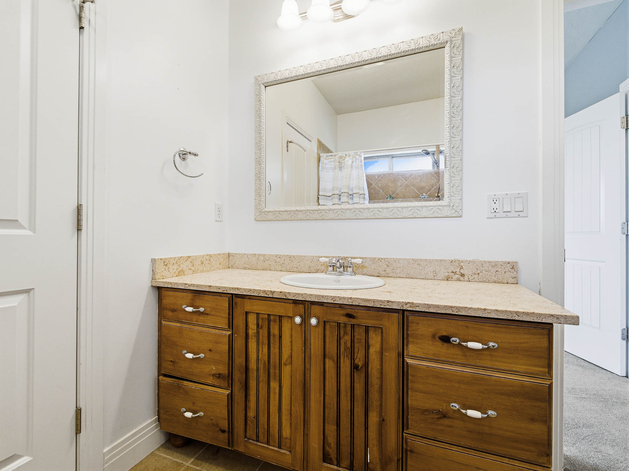 Vanity featuring a light-toned countertop with integrated sink, wood cabinetry, and a framed mirror