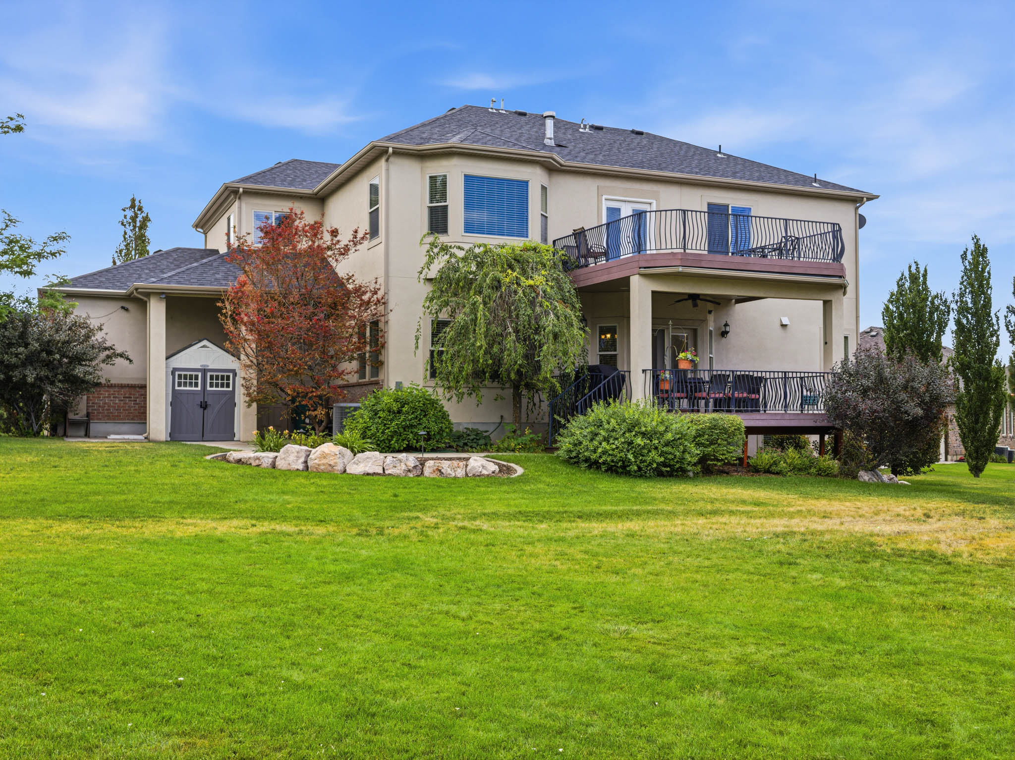Expansive green lawn bordering a two-story stucco exterior with a multi-level deck