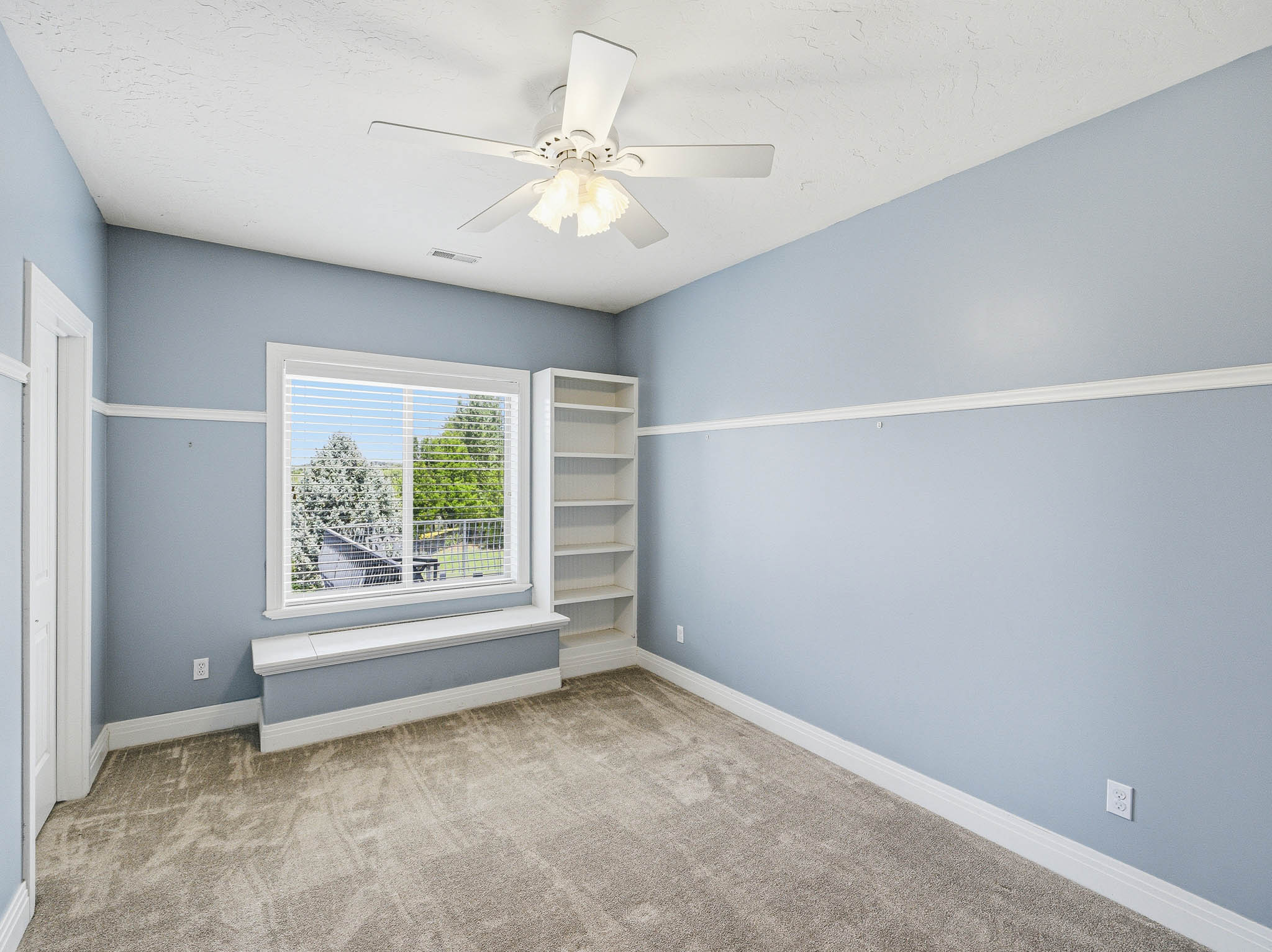 Carpeted room featuring a large window with blinds, a window seat, and built-in shelving