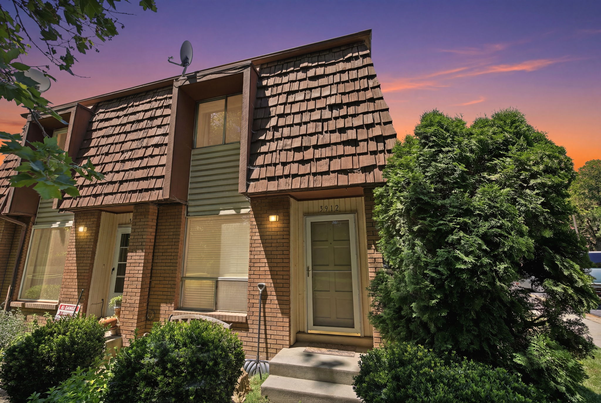 Townhome exterior featuring brick and siding facade, dimensional shingle roof, established evergreen landscaping, and front entry with steps