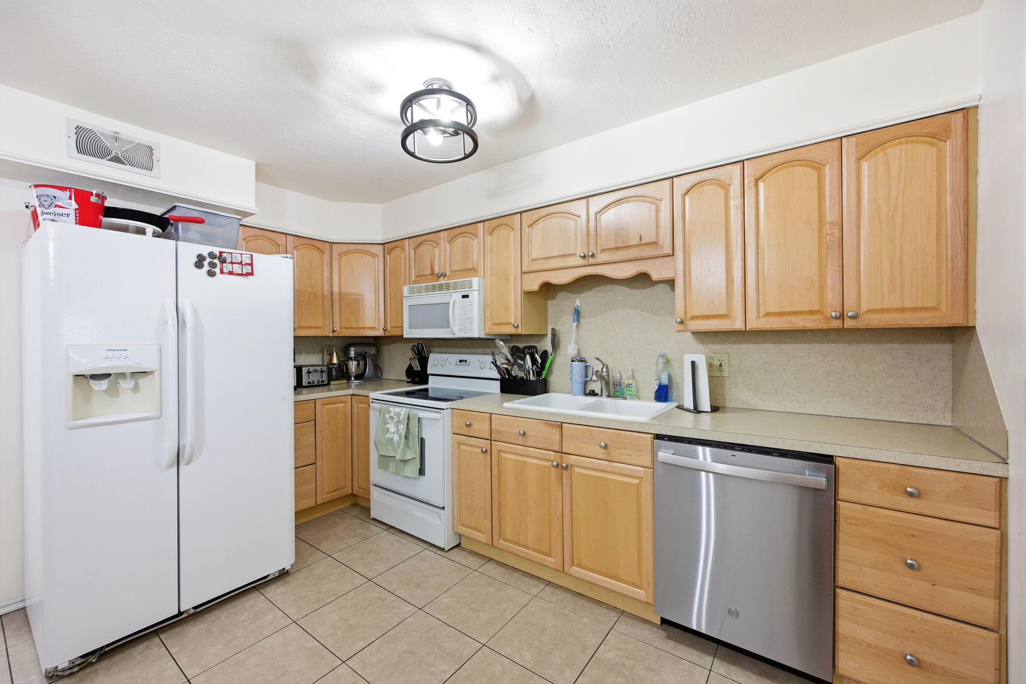 Kitchen featuring light wood cabinetry, light-toned countertops, ceramic tile flooring, a white drop-in sink, and a stainless steel dishwasher
