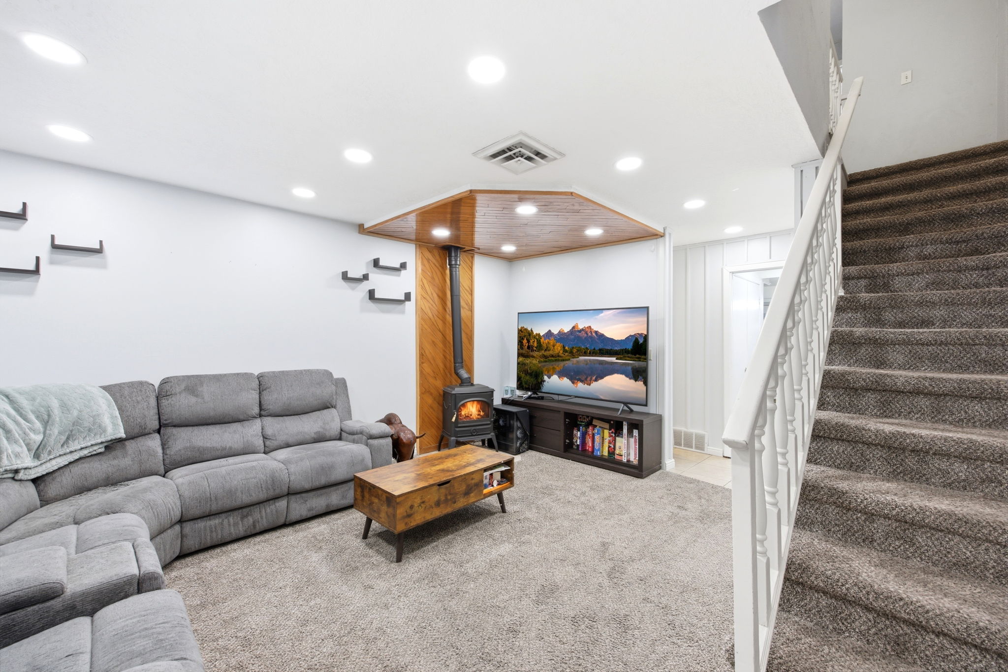 Carpeted living area featuring a wood-burning stove with a metal flue, recessed lighting, and a wood-paneled ceiling accent