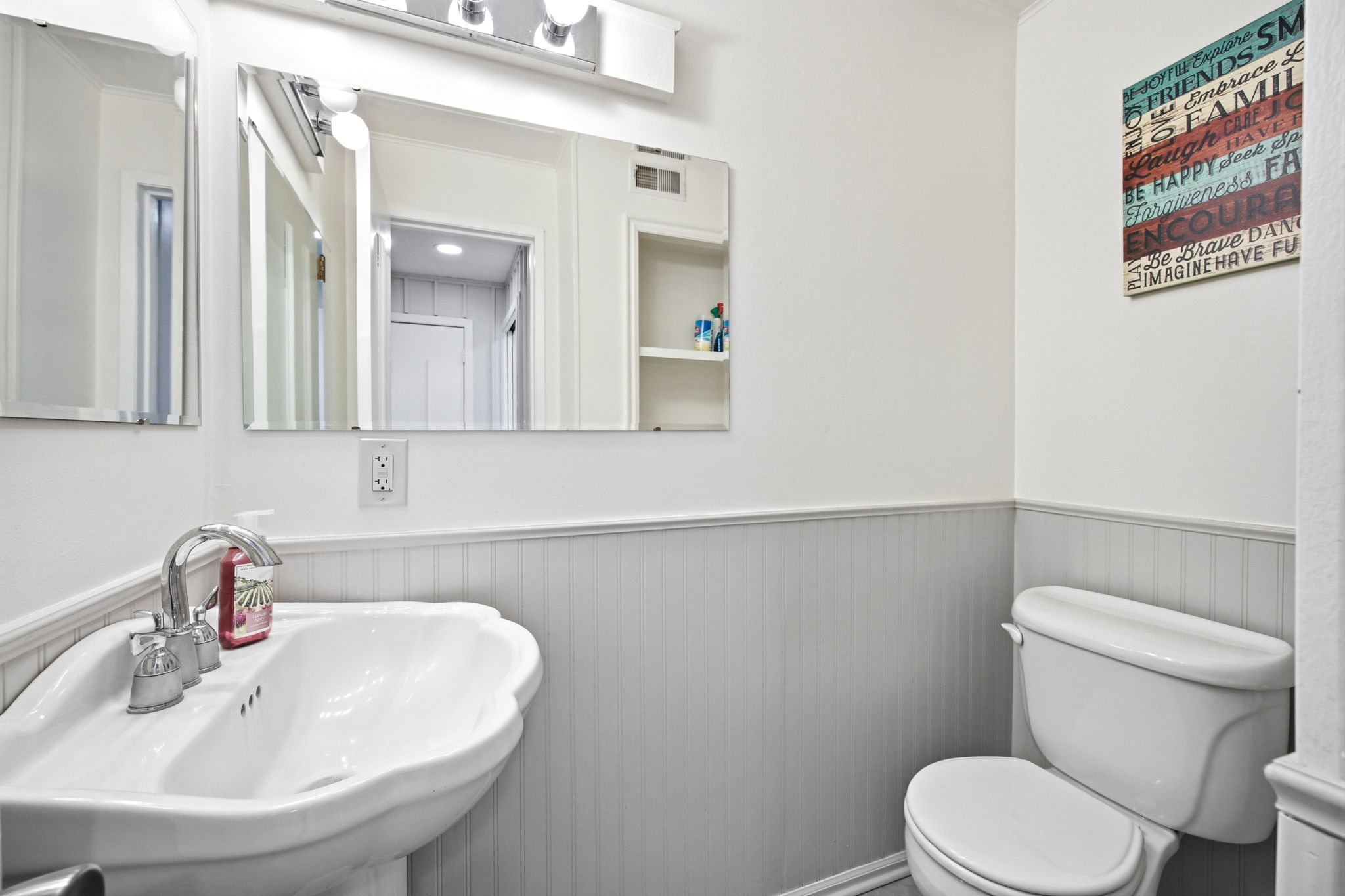Bathroom featuring a pedestal sink with chrome faucet, a toilet, and beadboard wainscoting