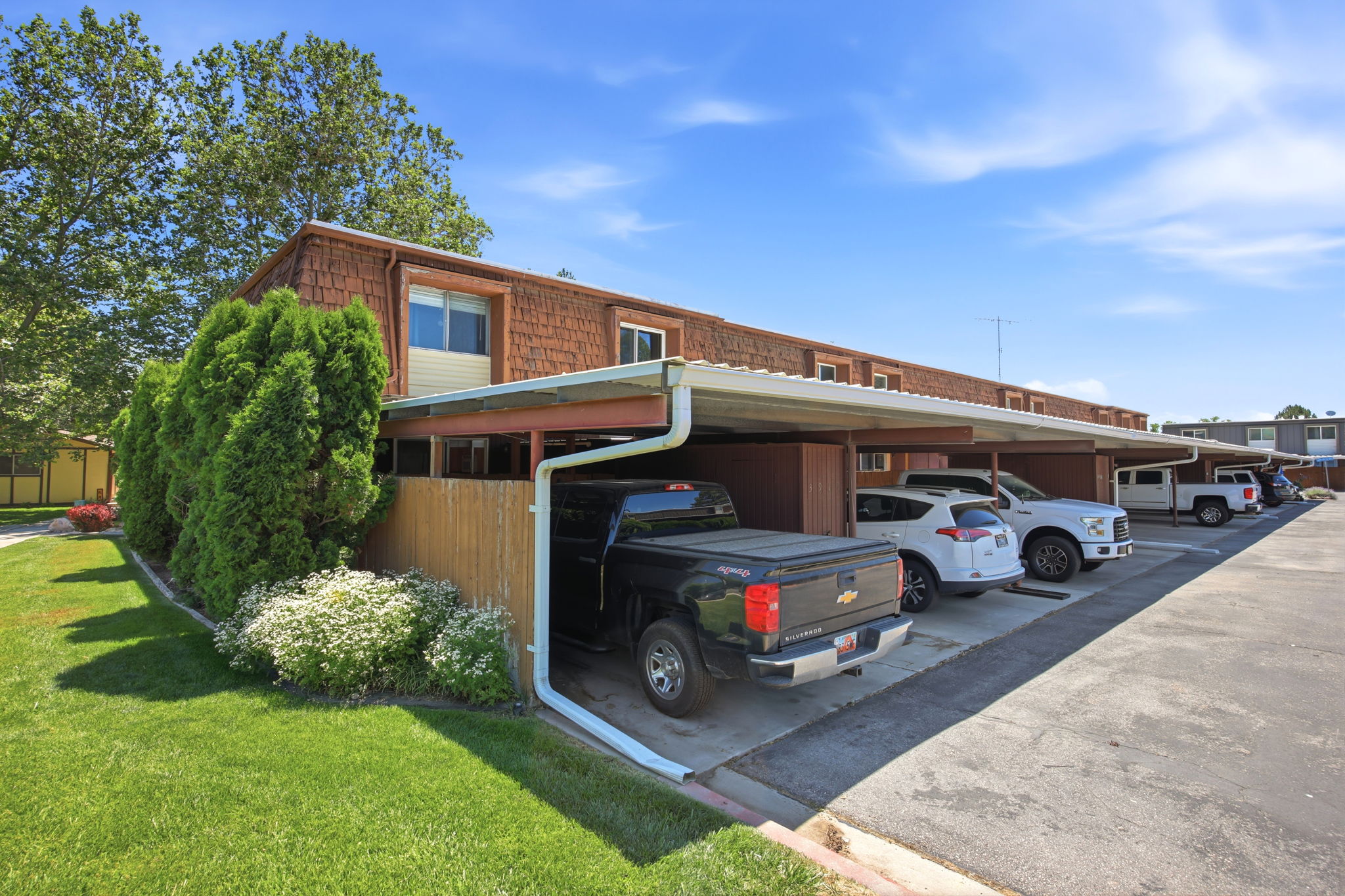 Exterior featuring wood shake siding, neutral vinyl siding accents, and a continuous covered parking structure