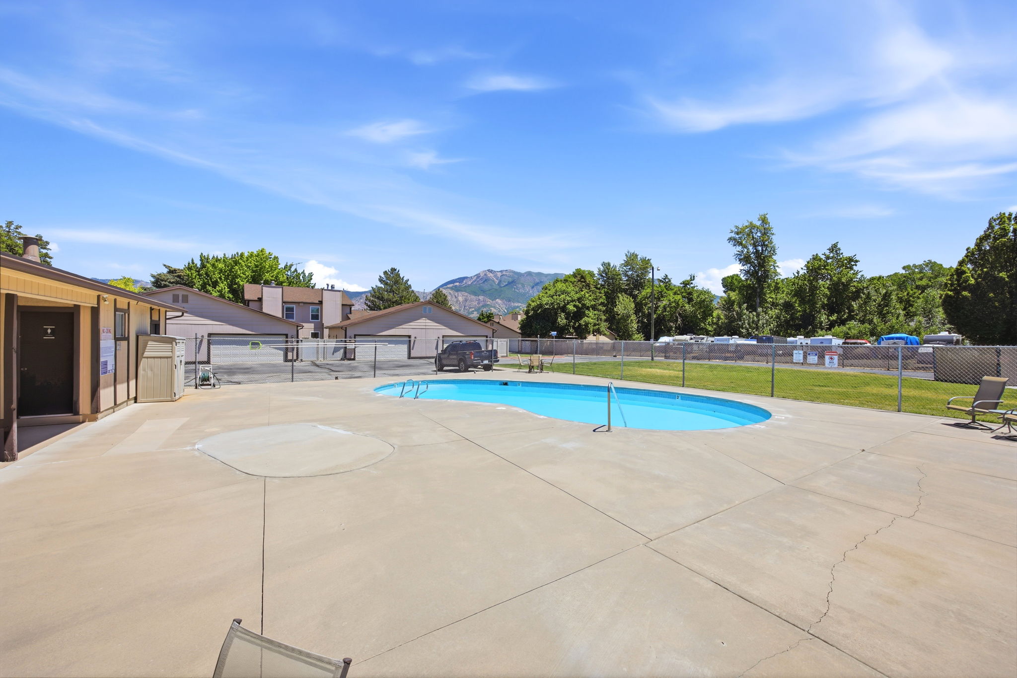 Community swimming pool with surrounding concrete decking, bordered by a chain-link fence and residential structures